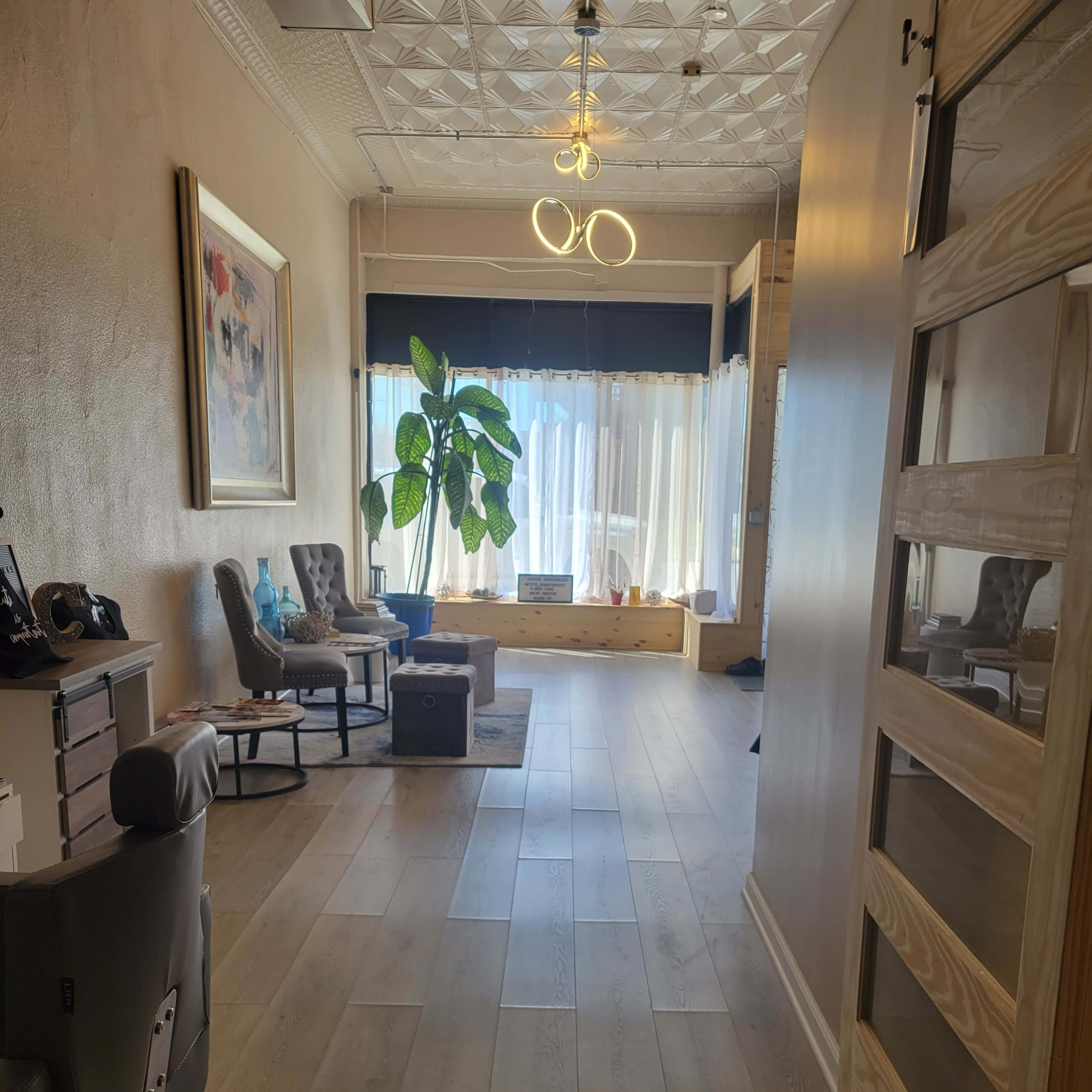A hallway with a plant, chairs, and a window letting in natural light.