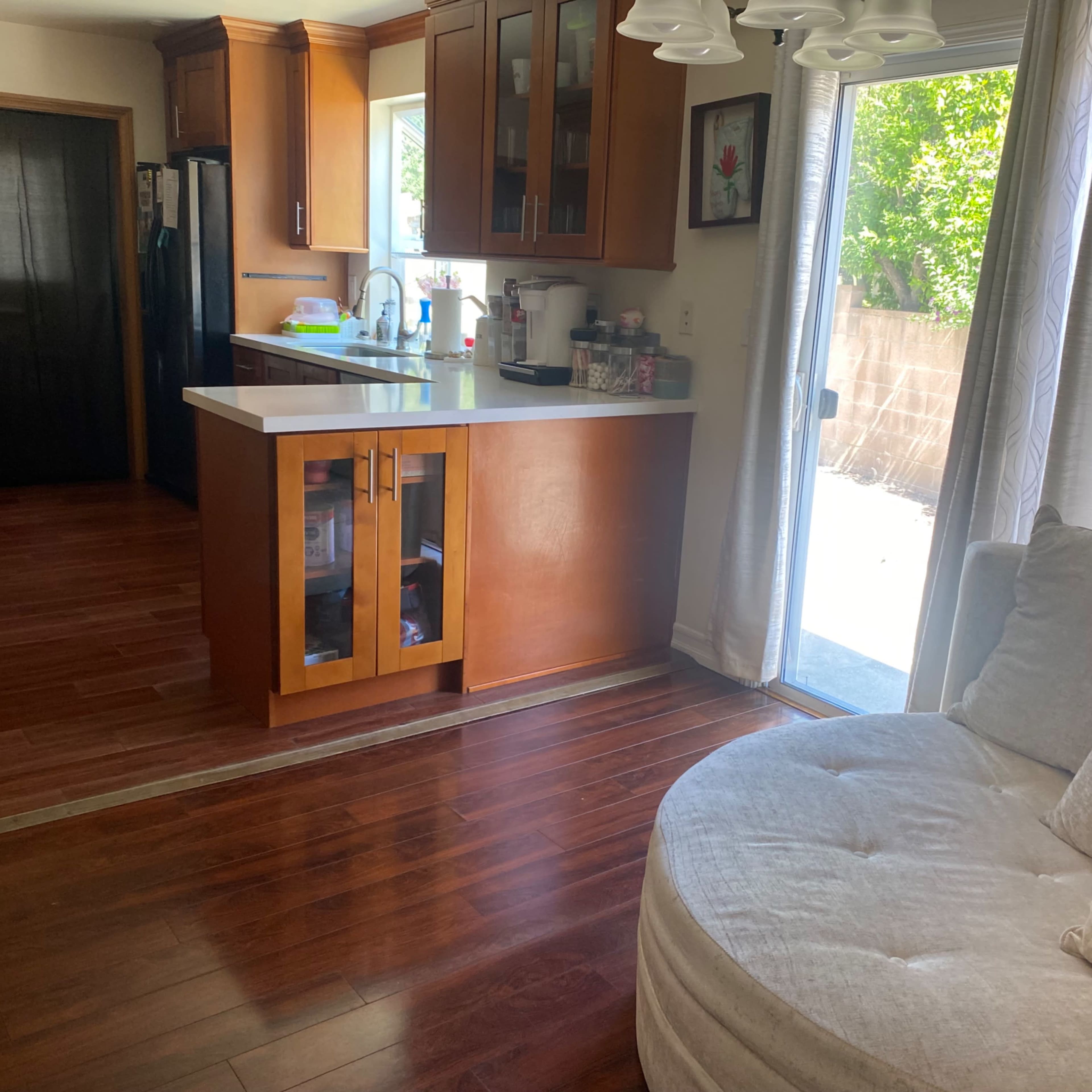 A cozy living area features a round, plush sofa beside a bright kitchen with wooden cabinets and a door leading to an outdoor space.