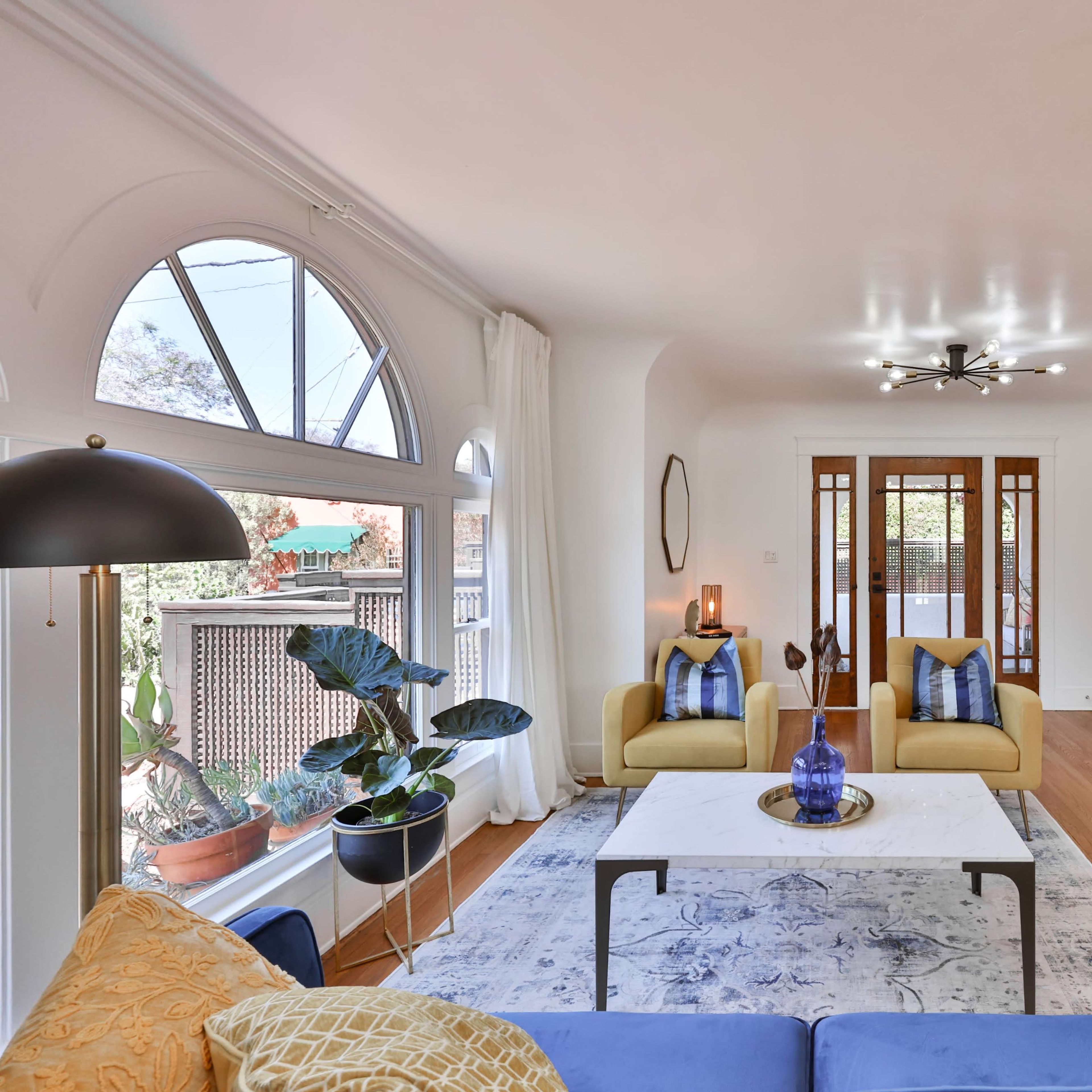 A bright living room featuring a blue sofa, yellow accent chairs, a coffee table, a fireplace, and large windows.