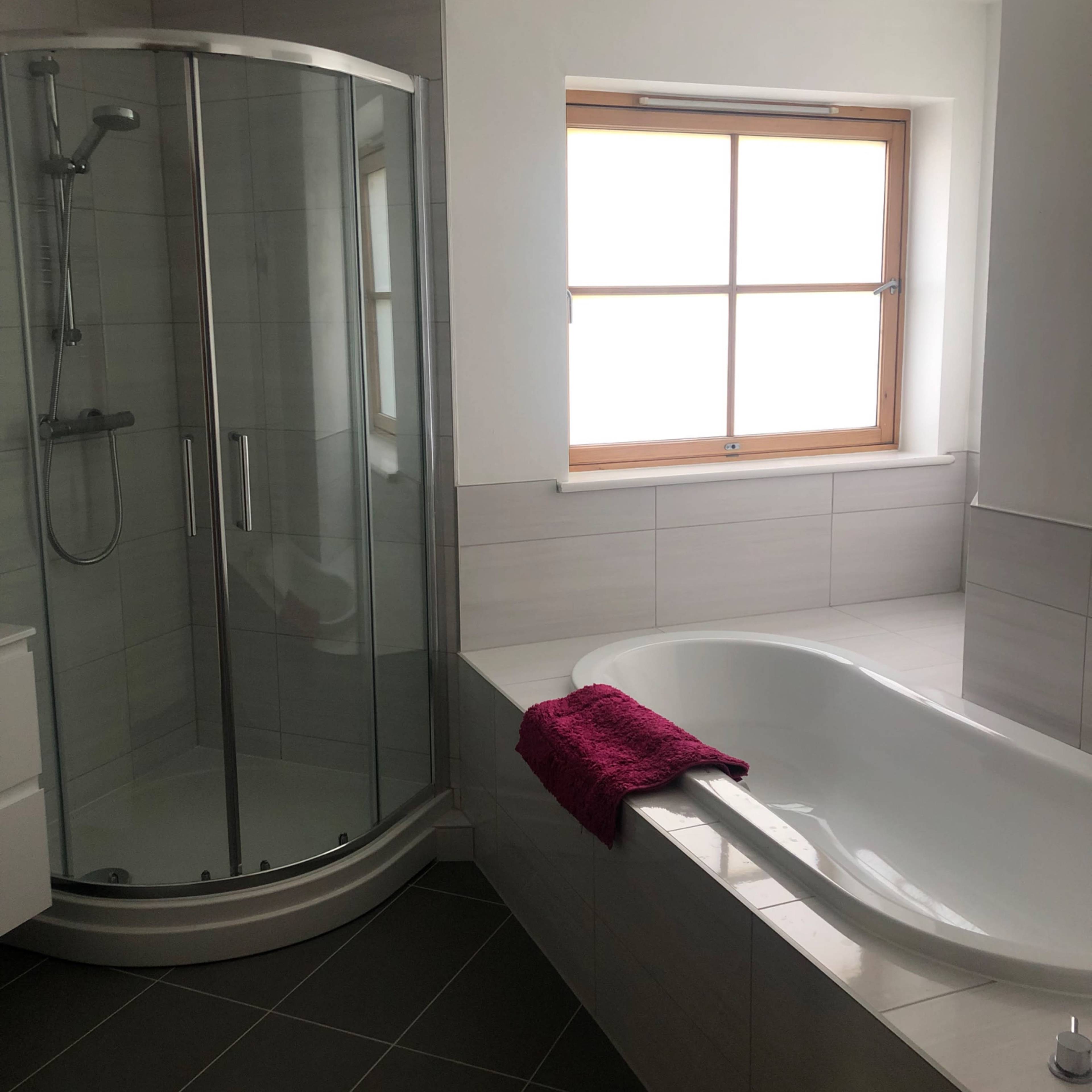 A modern bathroom featuring a glass shower stall and a white bathtub next to a window.