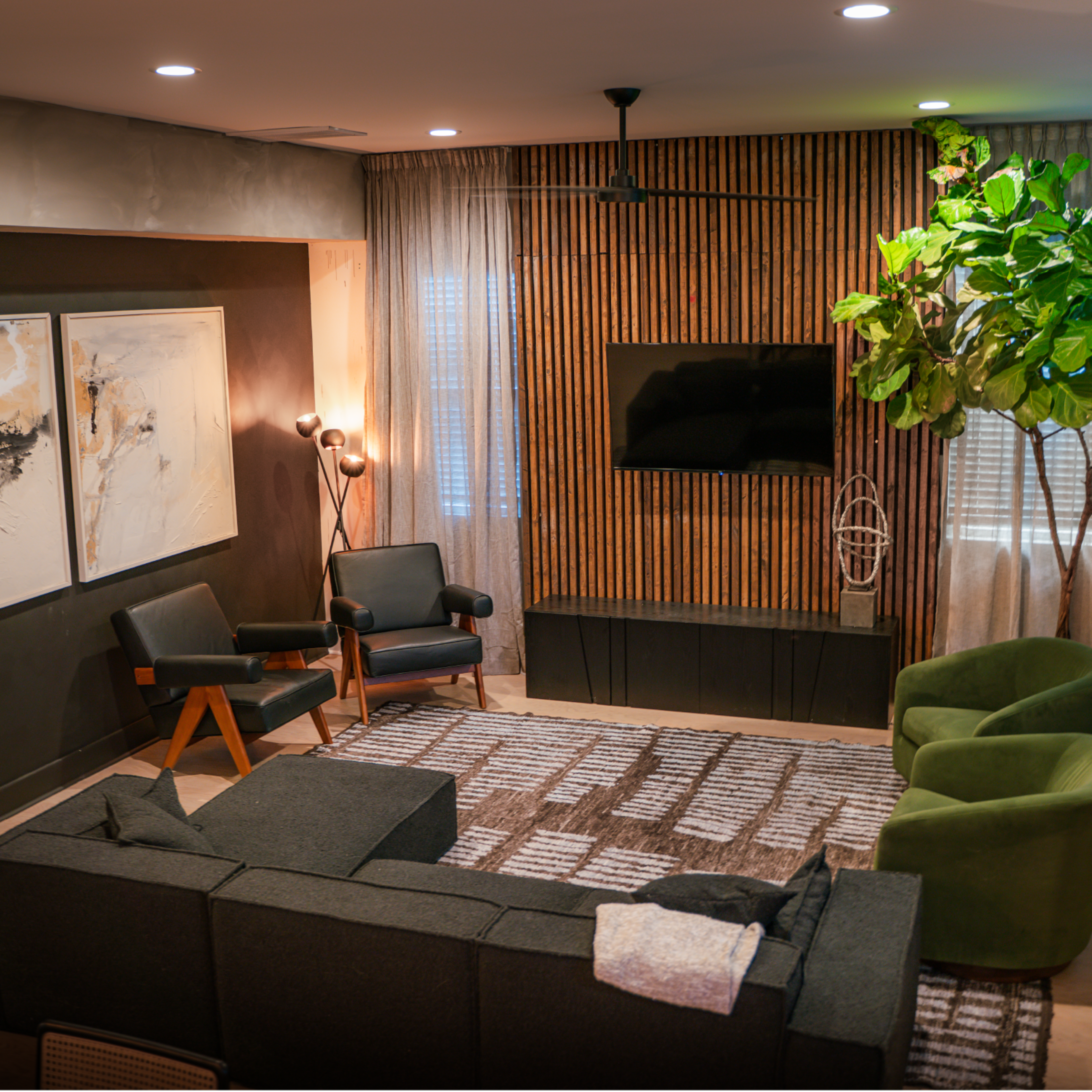 The living room features a sectional couch, two chairs, a large rug, a flat-screen TV mounted on a wooden accent wall, and a potted plant in the corner.