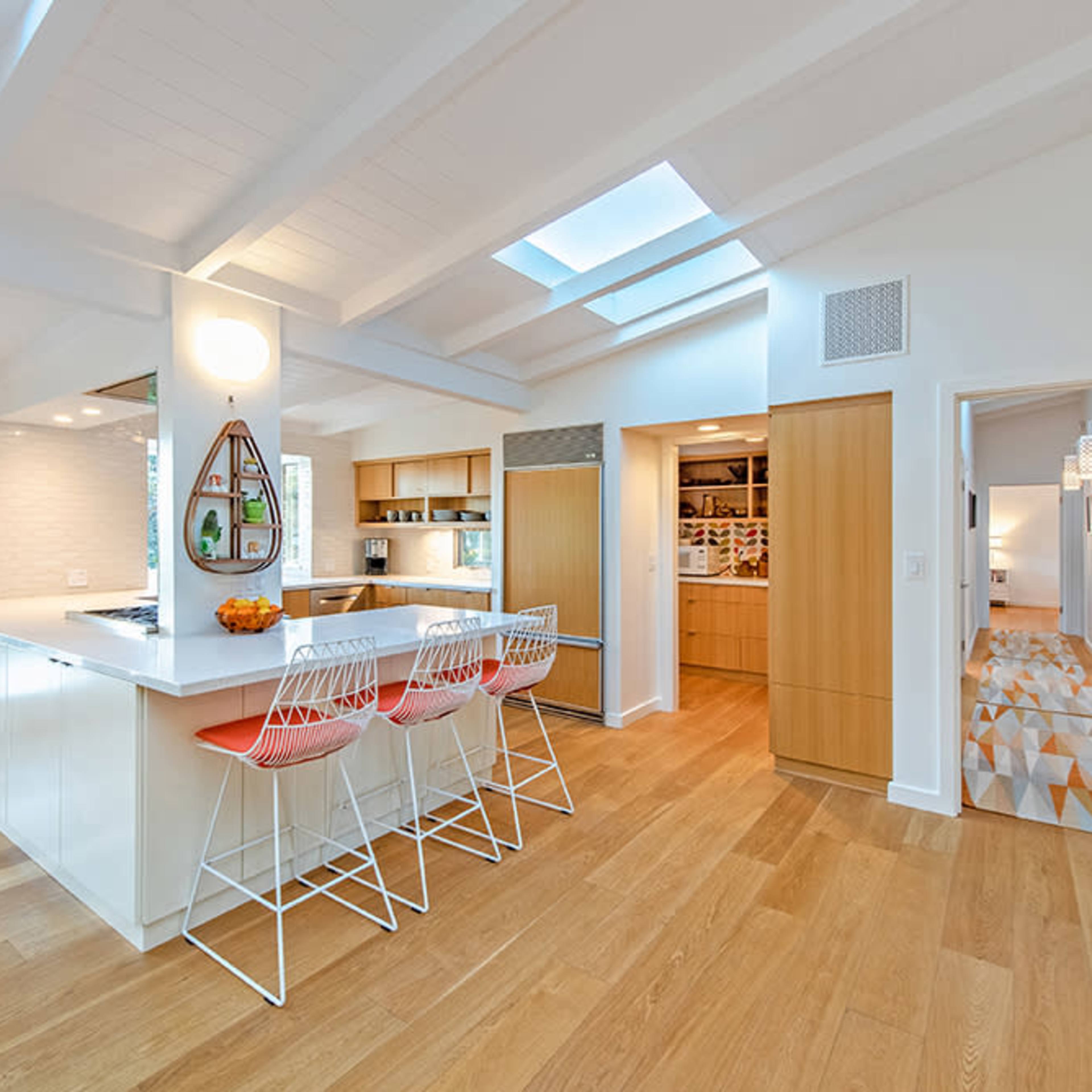 A modern kitchen with a central island and three wire bar stools, illuminated by natural light from a skylight above.