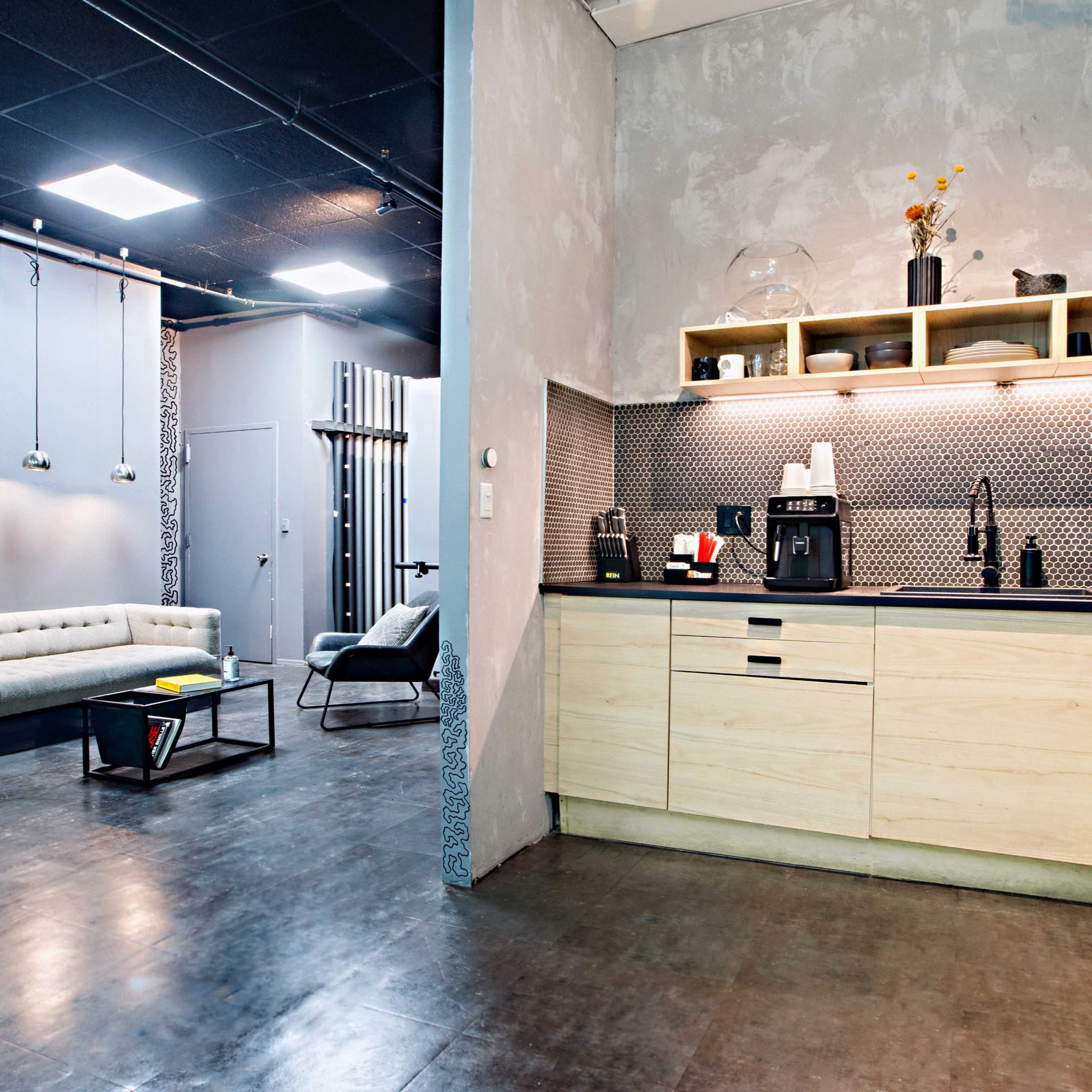 A modern kitchen area with wooden cabinets, a coffee maker, and a gray sofa in a seating area adjacent to it.