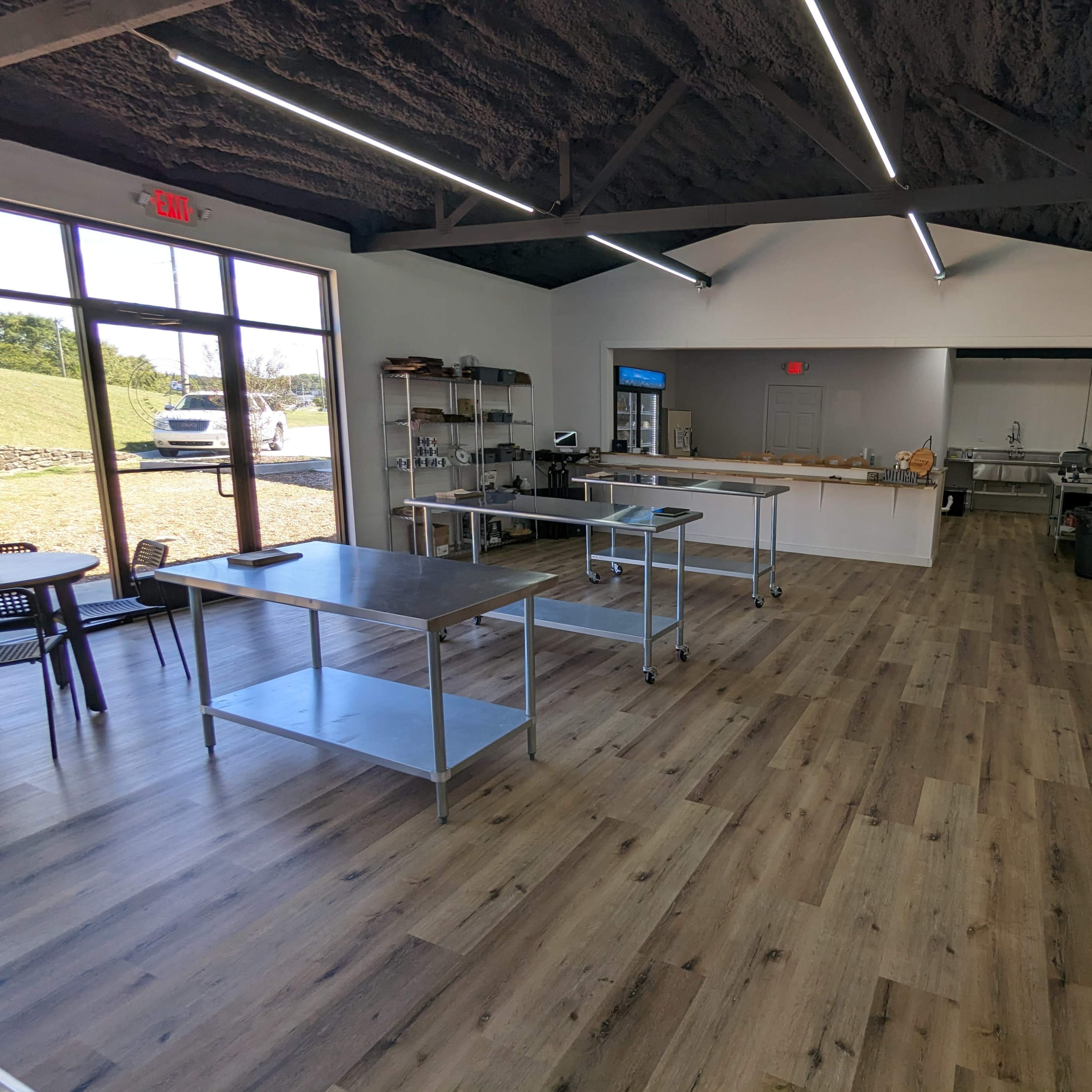 A spacious, modern interior of a commercial kitchen with stainless steel tables, equipment, and a large open area featuring wooden flooring and a ceiling with visible beams.