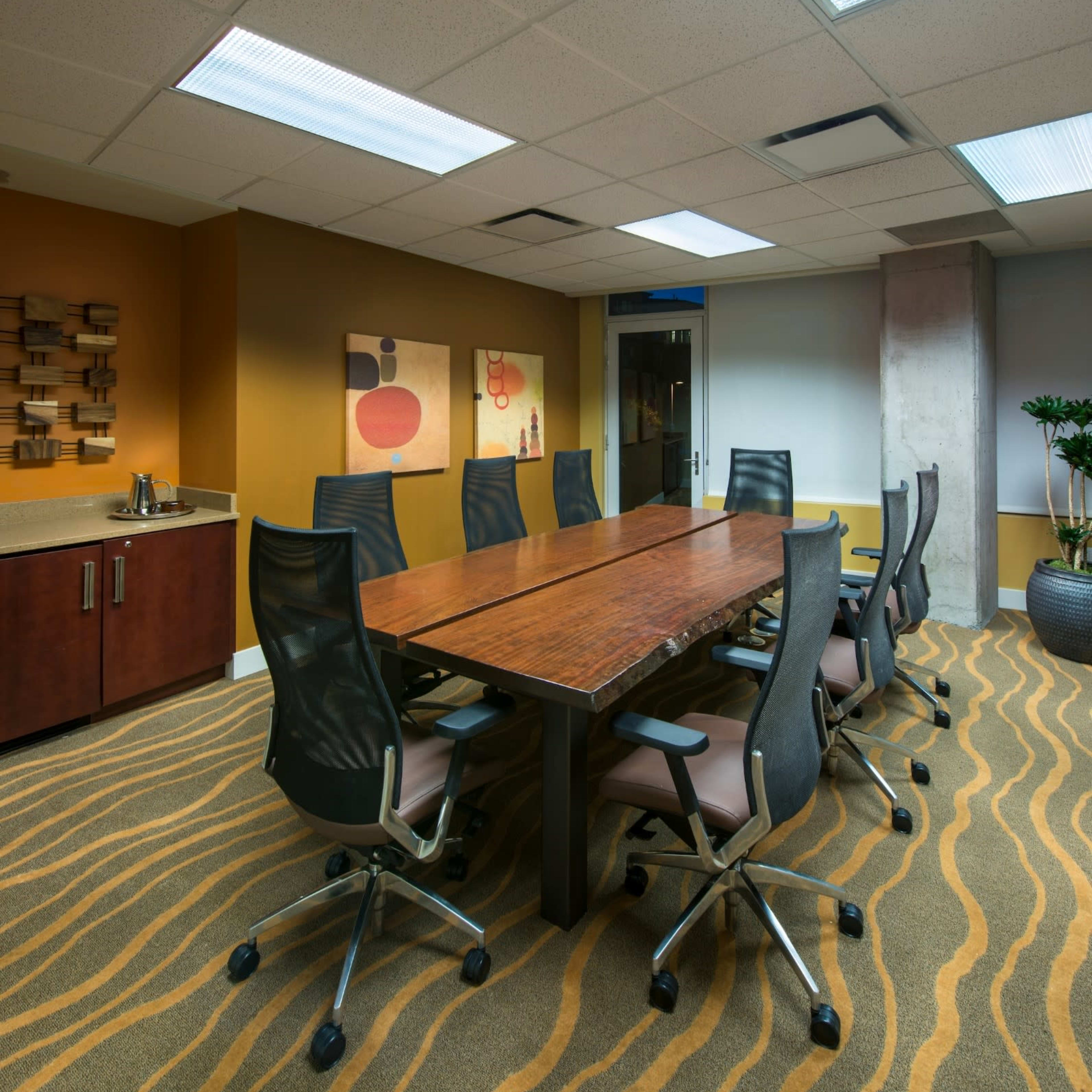 A modern conference room with a long wooden table surrounded by office chairs and a patterned carpet.