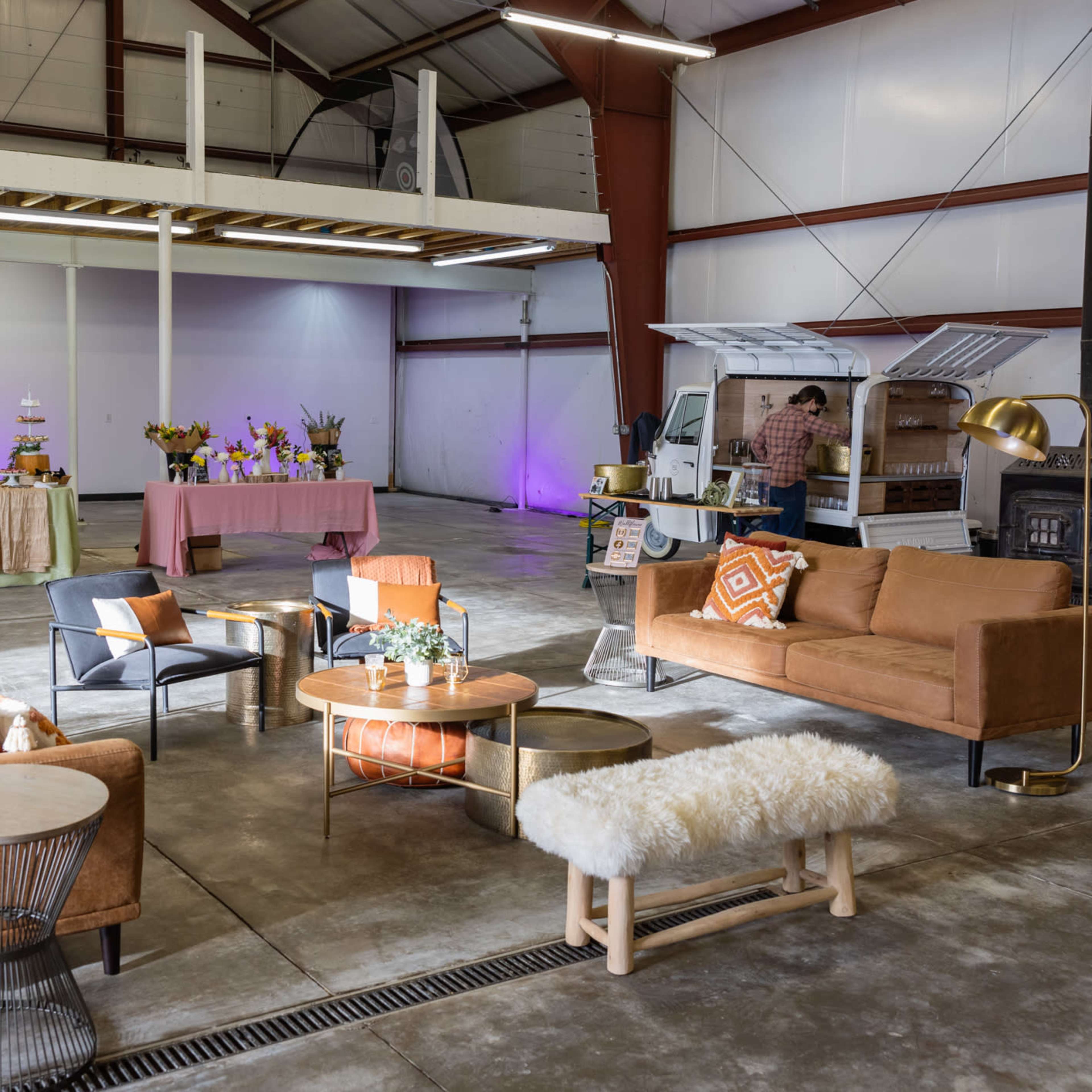 A spacious indoor area with a seating arrangement of various lounge furniture, decorative tables, and event setup in the background.
