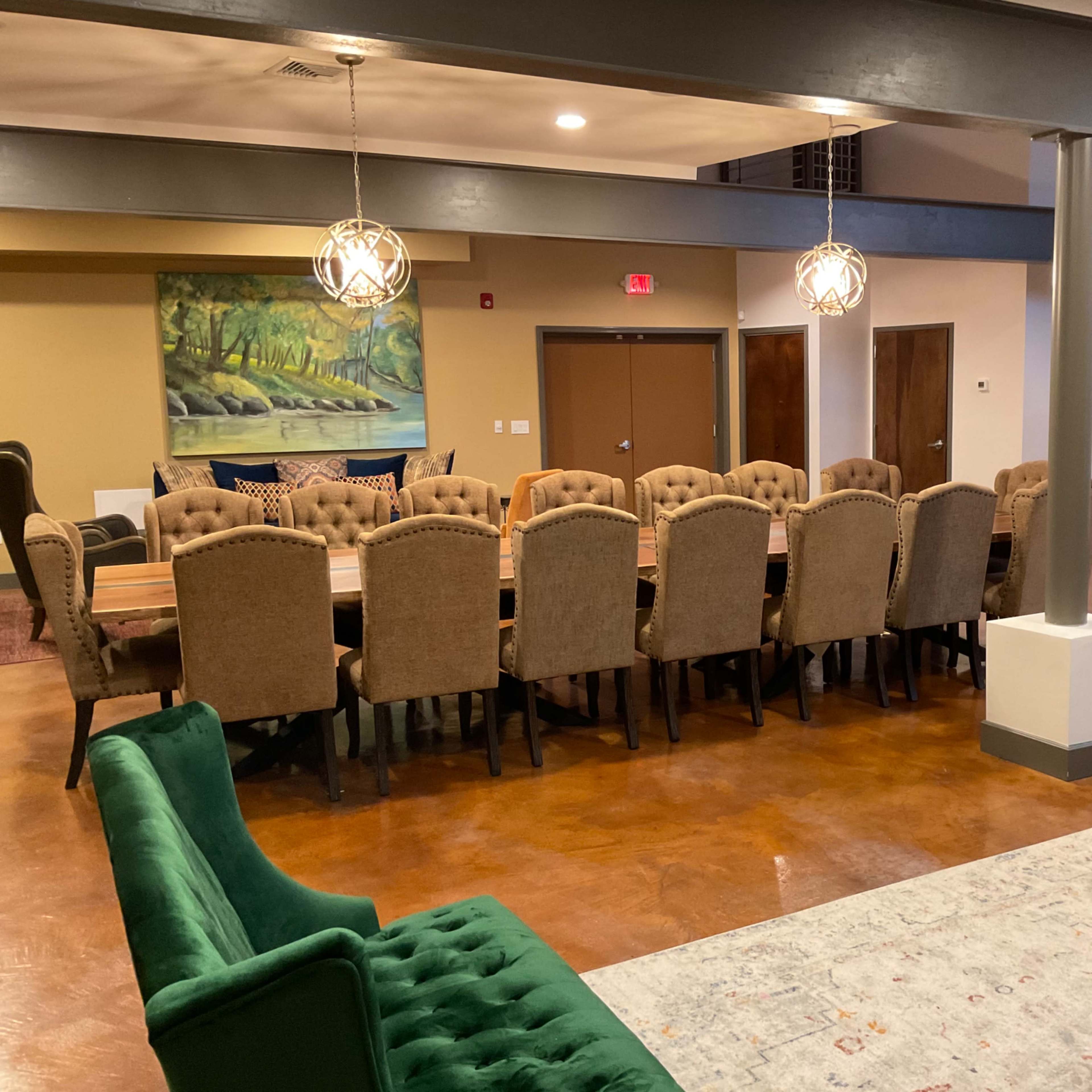 A spacious meeting room with a long wooden table surrounded by upholstered chairs, complemented by a colorful armchair and a decorative rug.