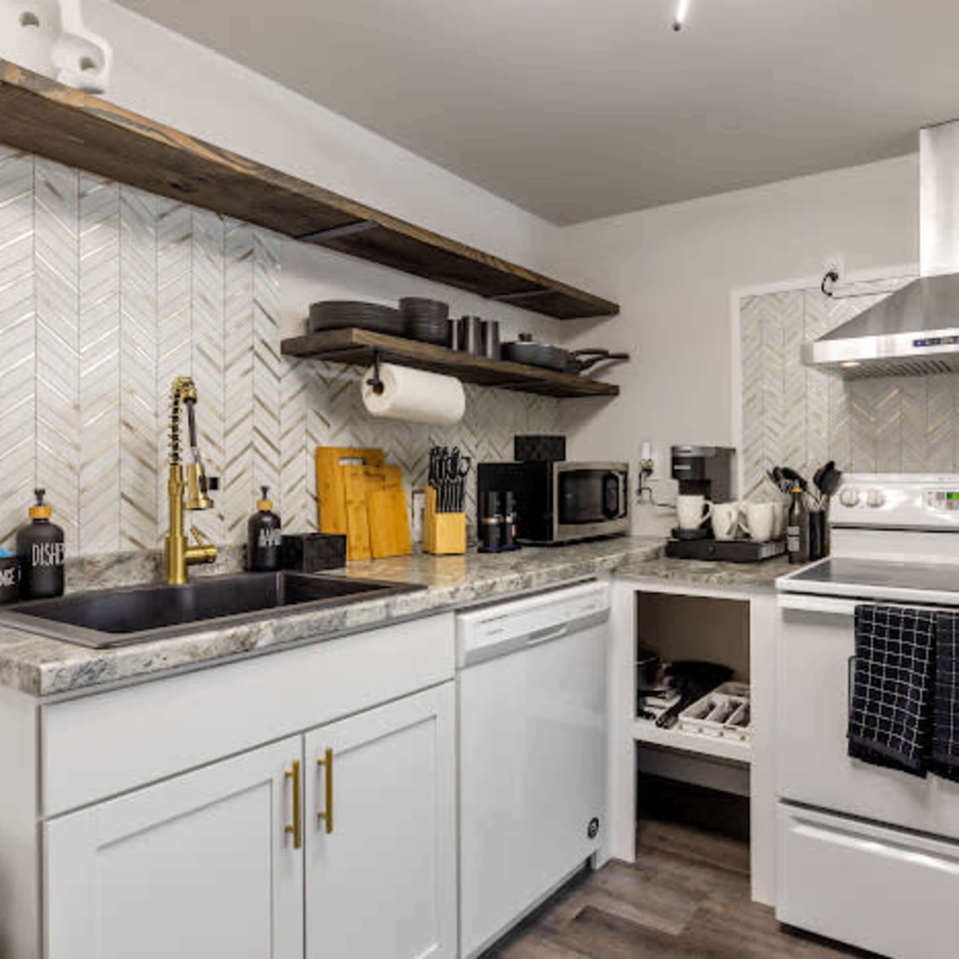 A modern kitchen featuring stainless steel appliances, white cabinetry, and open shelves with various kitchen utensils and containers.