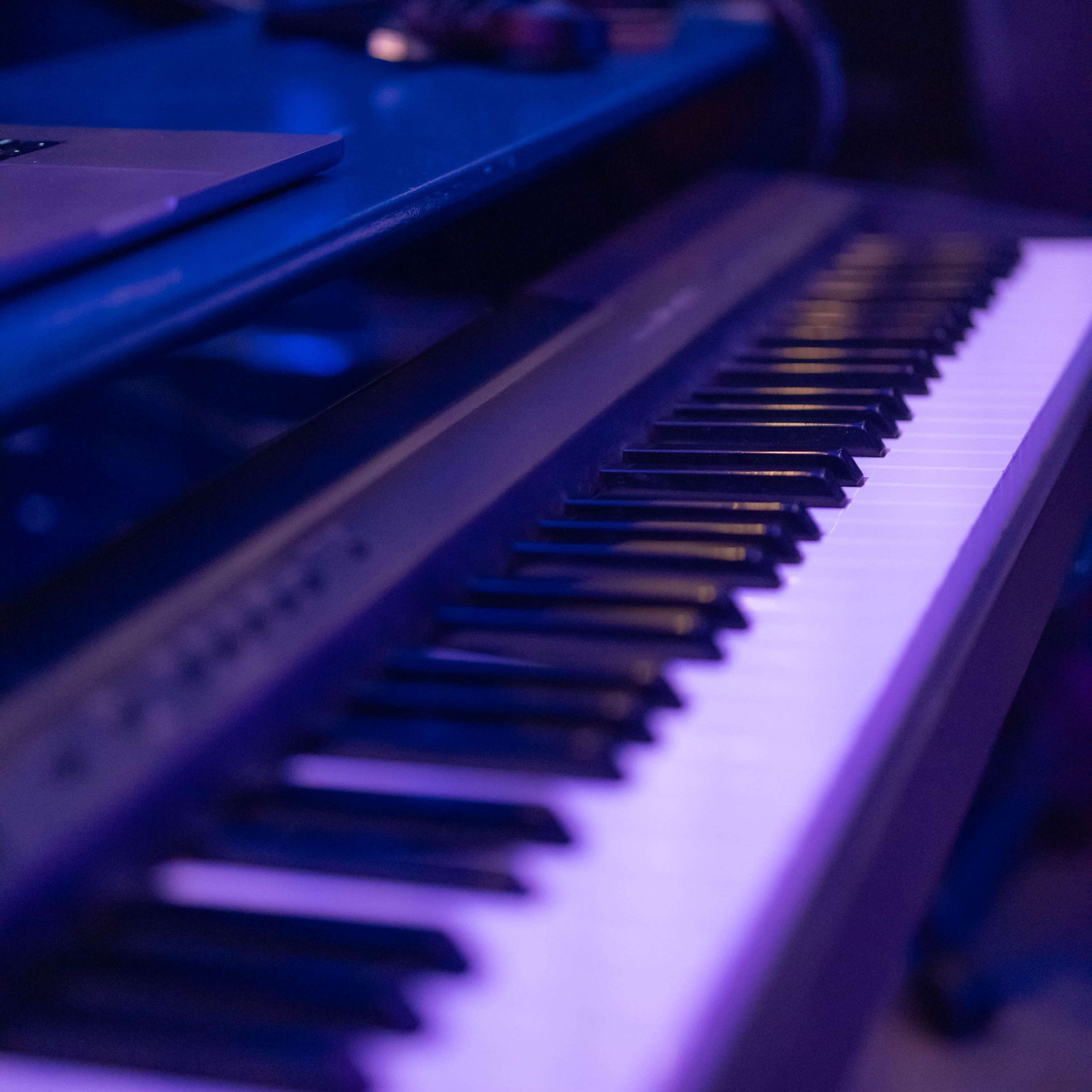 A close-up of a digital piano keyboard on a dark surface, illuminated by blue lighting.
