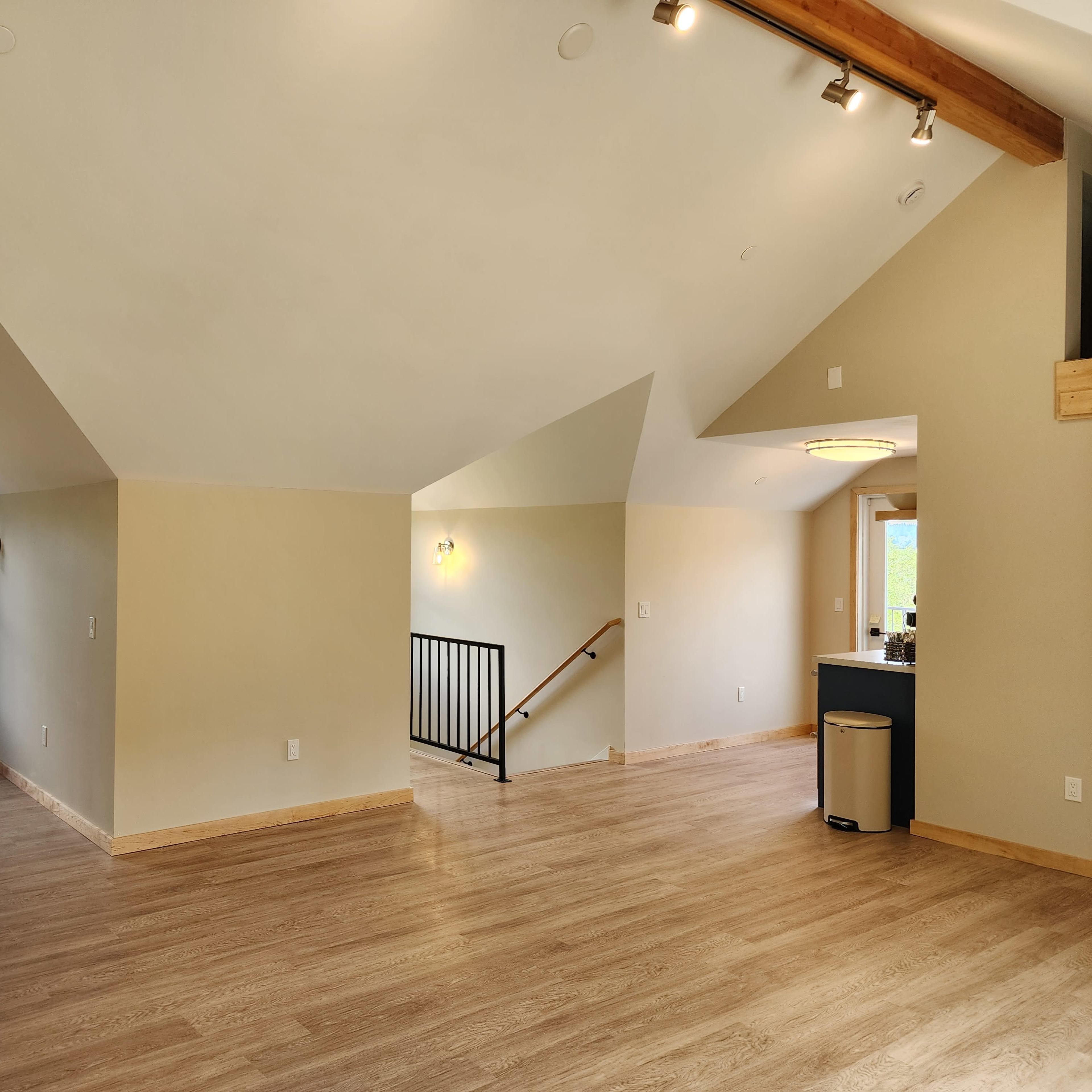 A spacious, well-lit room with sloped ceilings, wooden flooring, and an open layout adjacent to a staircase.