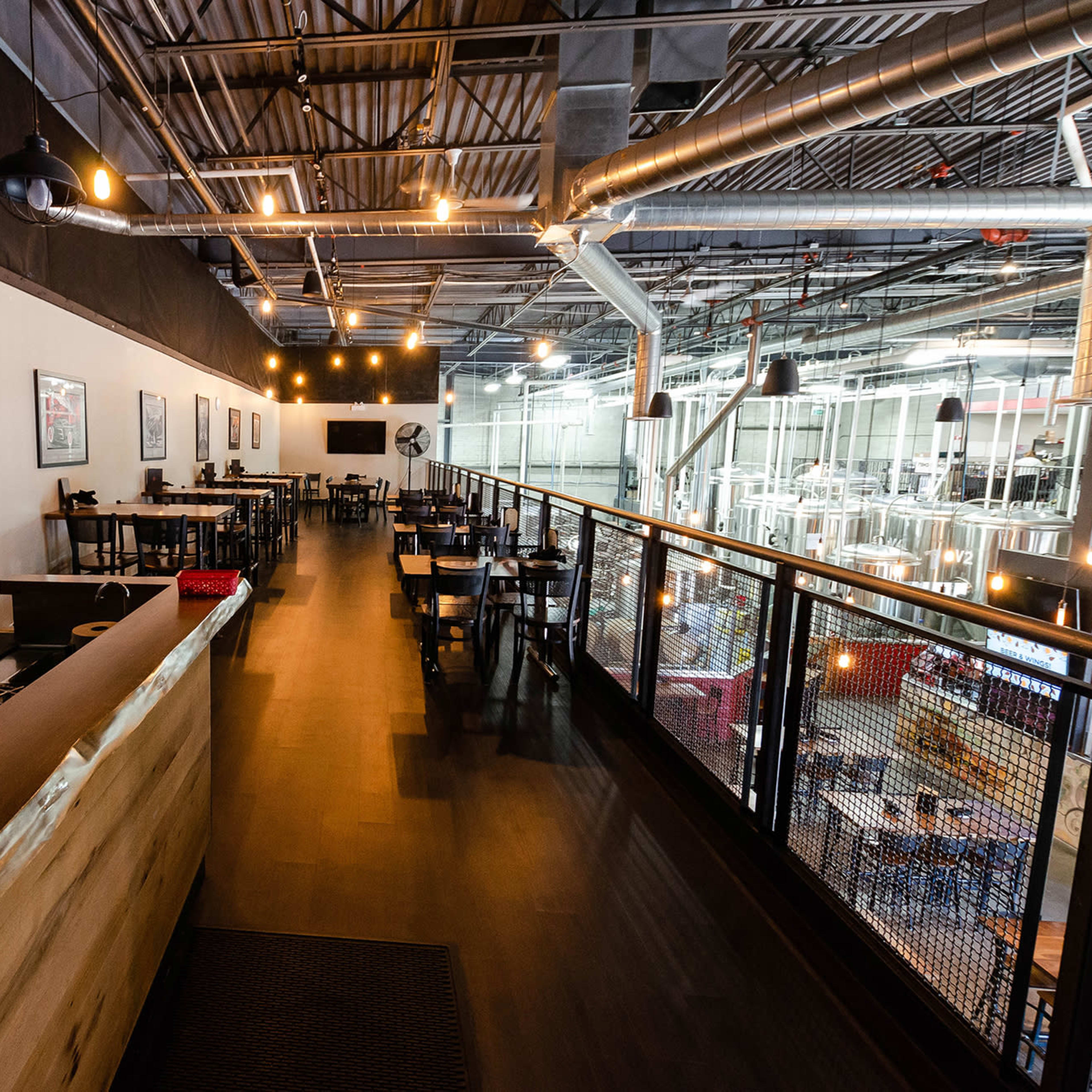 A spacious restaurant interior with a bar area, tables, and a view of brewing equipment in the background.