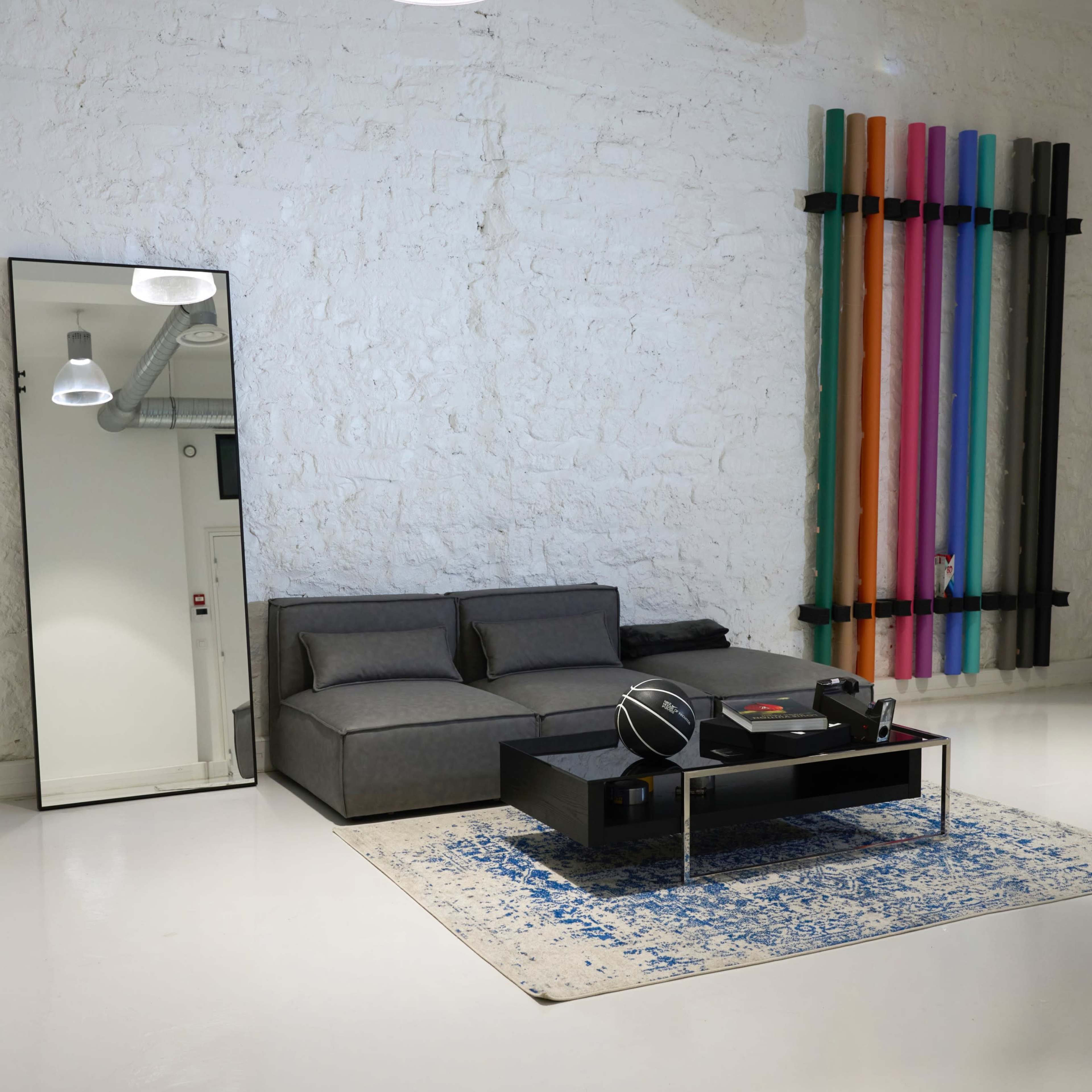 The room features a gray sofa, a low coffee table with a record player, a large mirror, and colorful vertical decorations against a white wall.