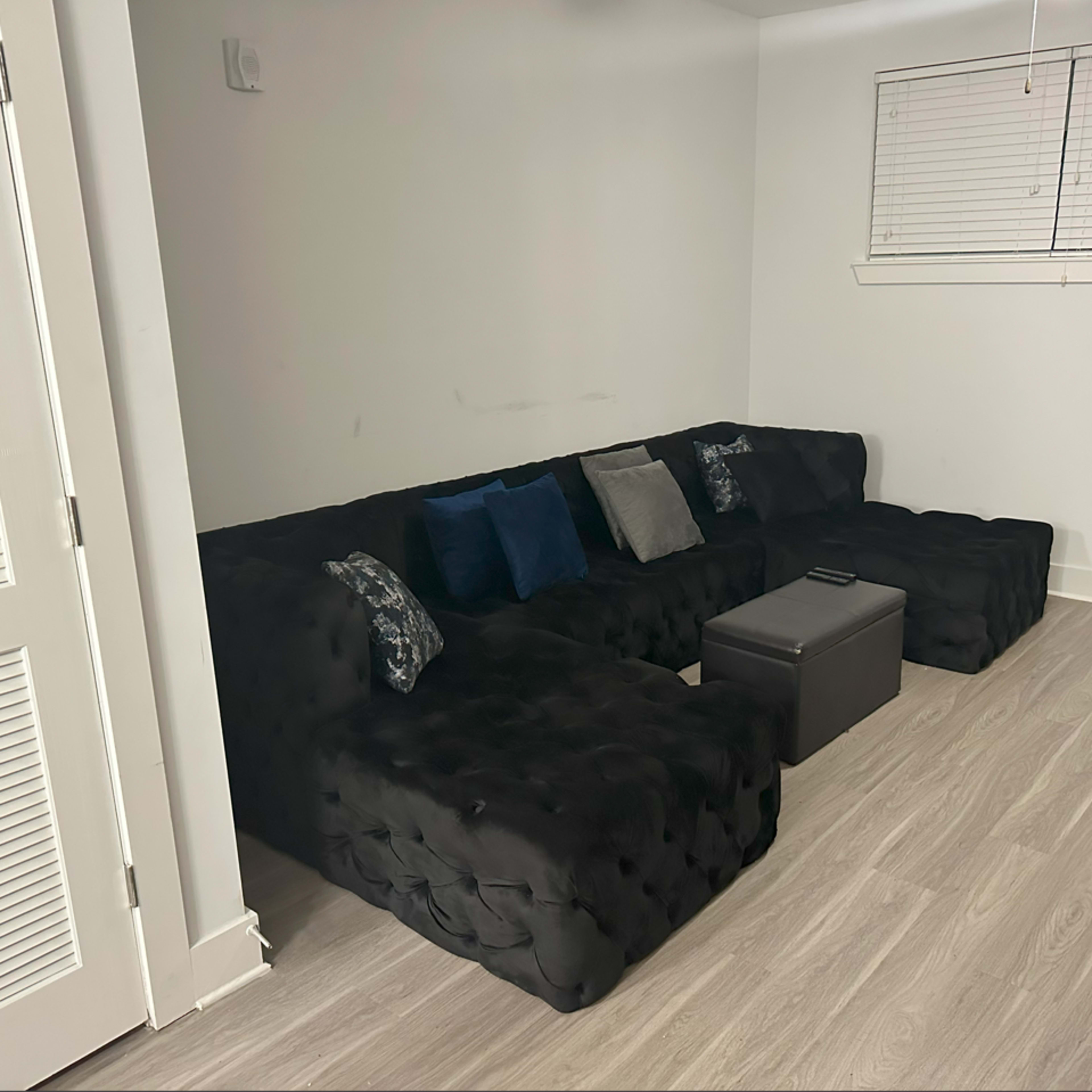 A semi-furnished room features a black sectional sofa with decorative pillows and a small black table in front of it.