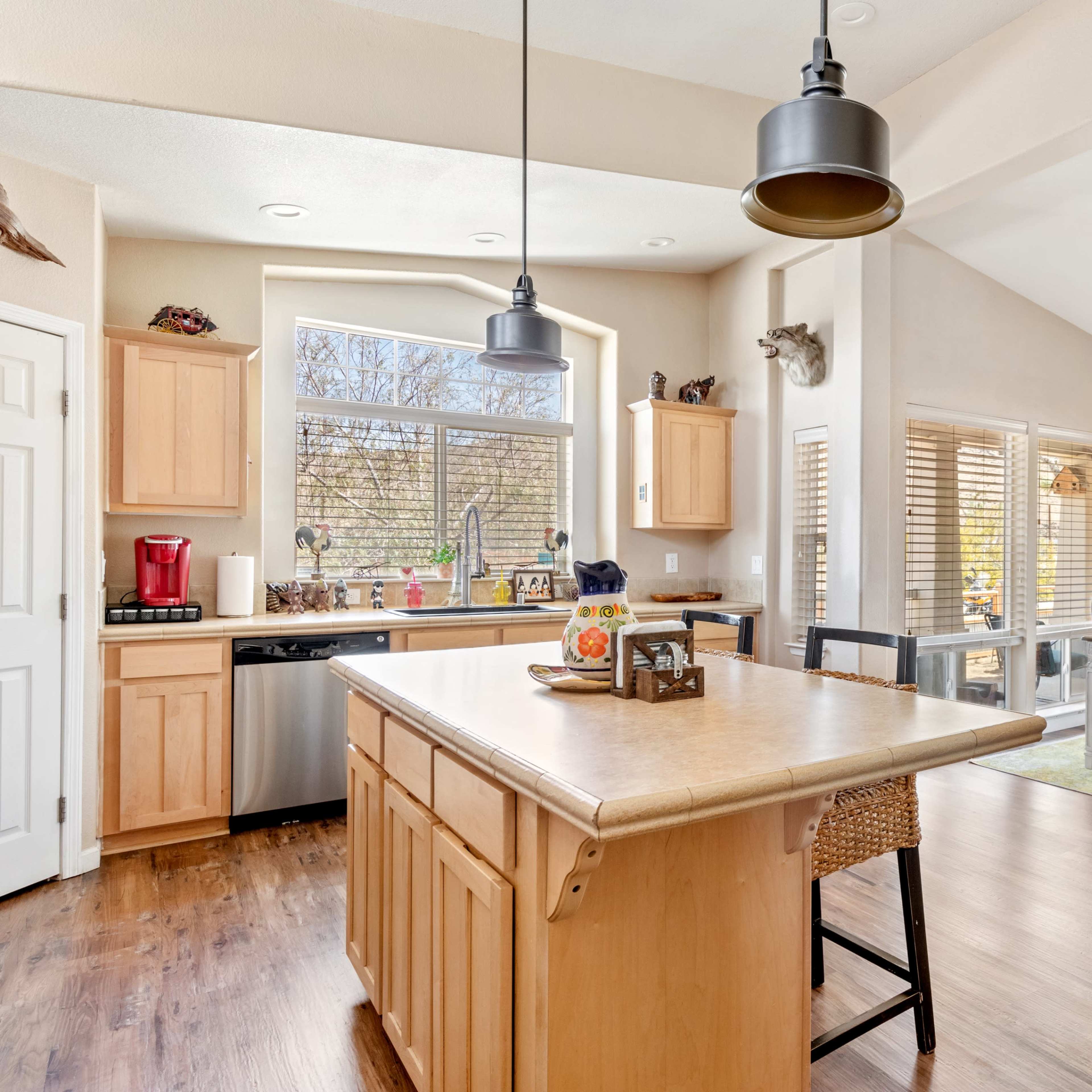 A spacious kitchen with wooden cabinets, a central island, and a dining area featuring large windows and a table set for several people.