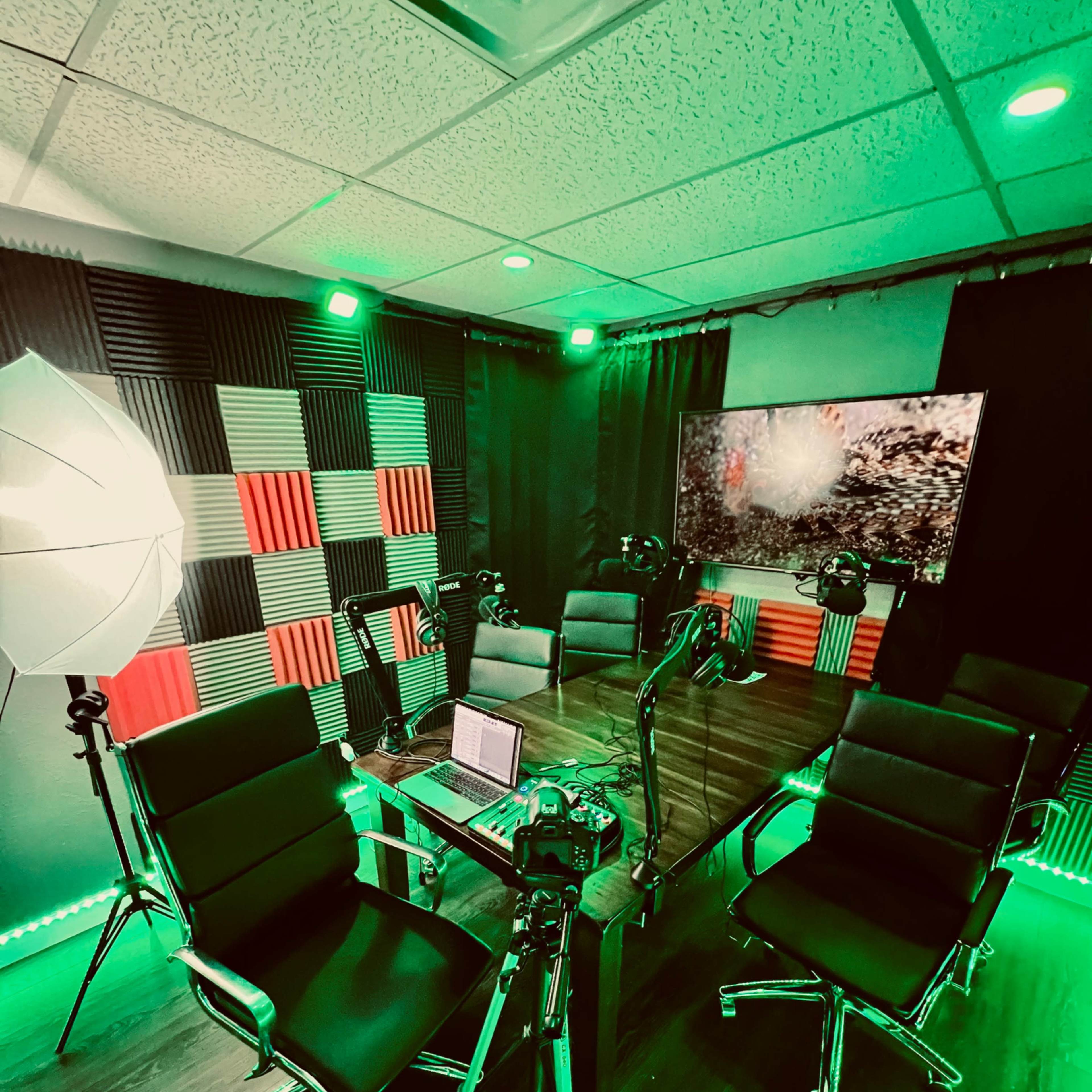 A modern studio setup with a large wooden table surrounded by black chairs, equipped with multiple cameras and lighting, and featuring green ambient lighting and a patterned backdrop.