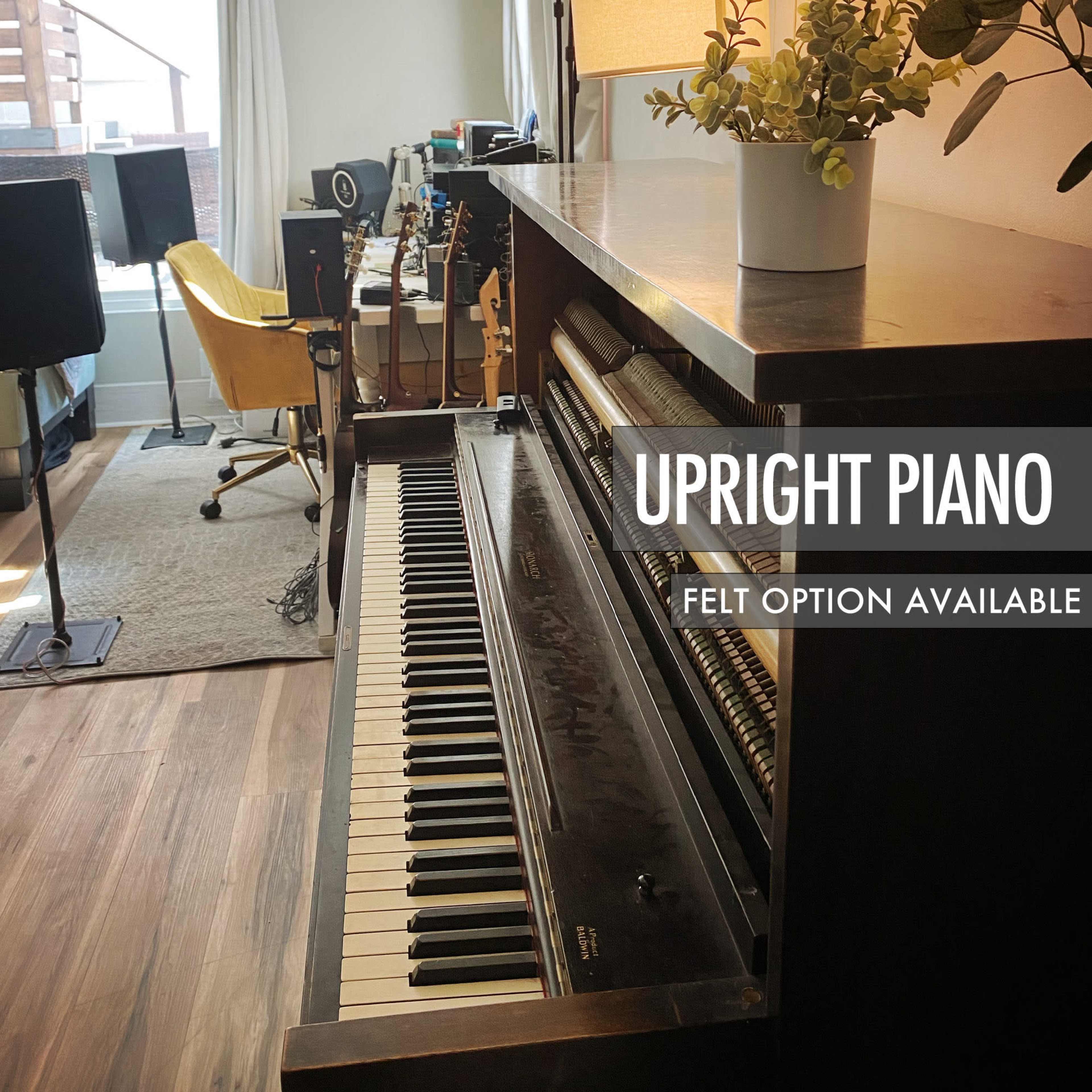 An upright piano is positioned near a window in a room with guitars and audio equipment visible in the background.