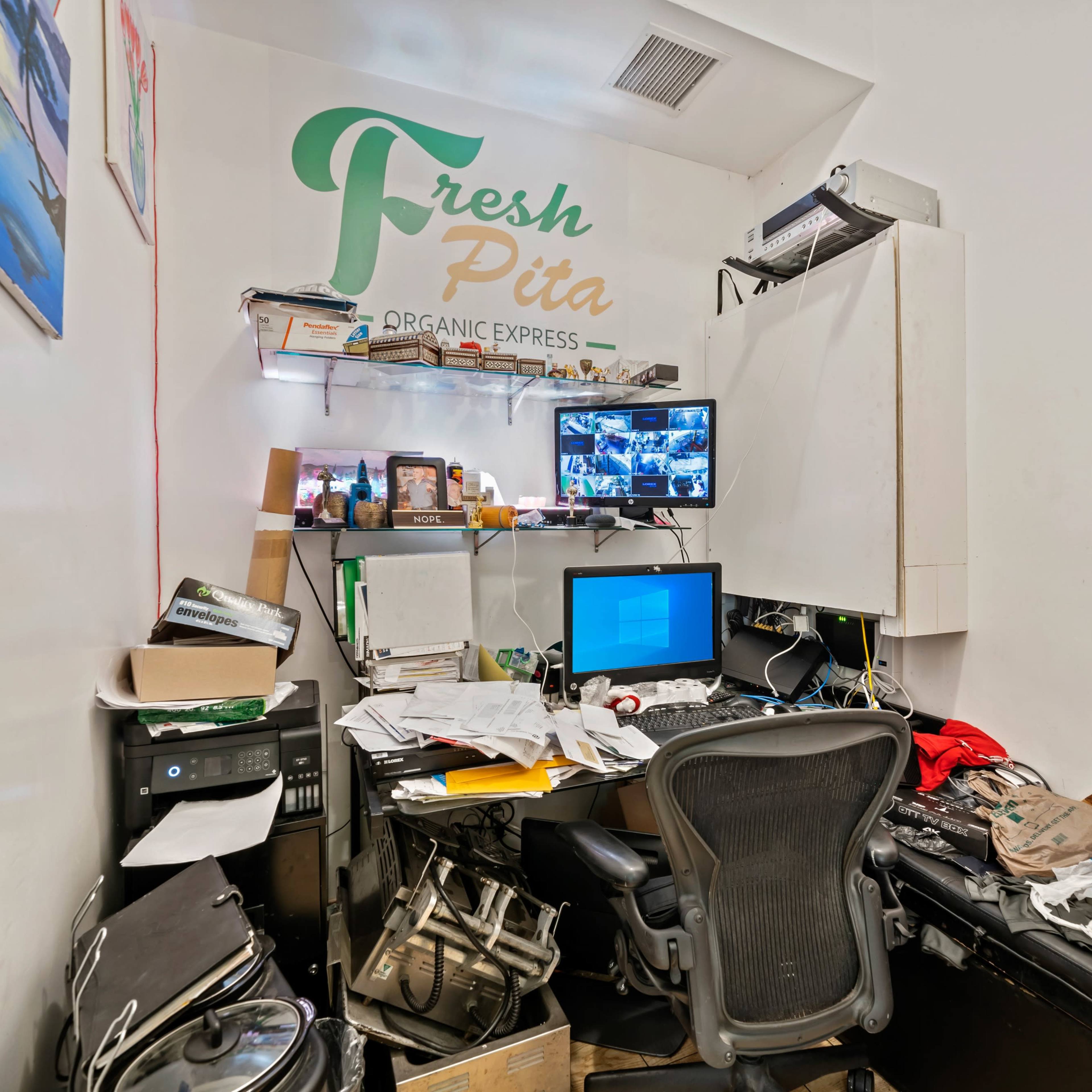 A cluttered office space with a desk piled high with papers and a computer monitor displaying surveillance footage.