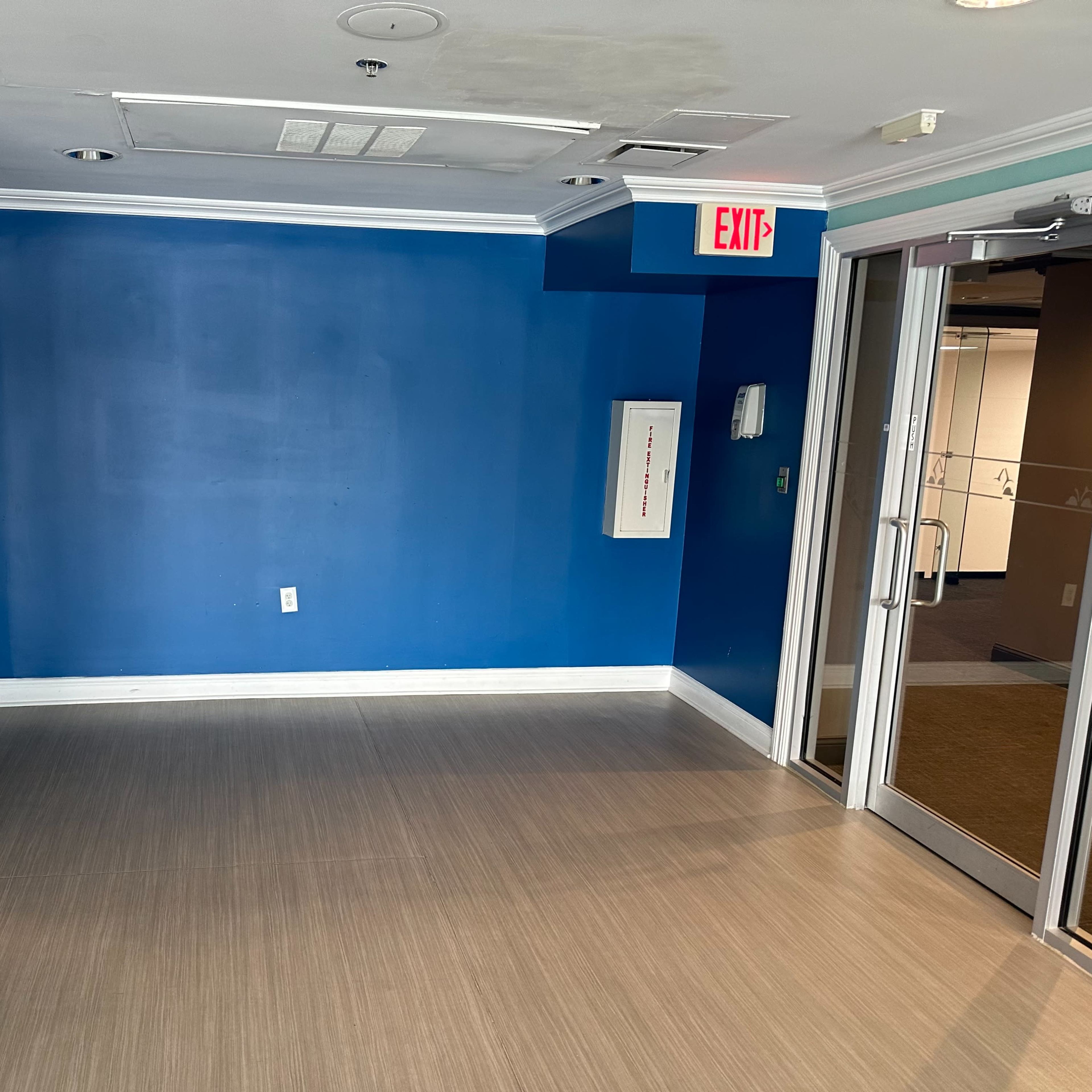 A small, empty room with a blue wall, a white exit sign, and two doorways leading to adjacent areas.