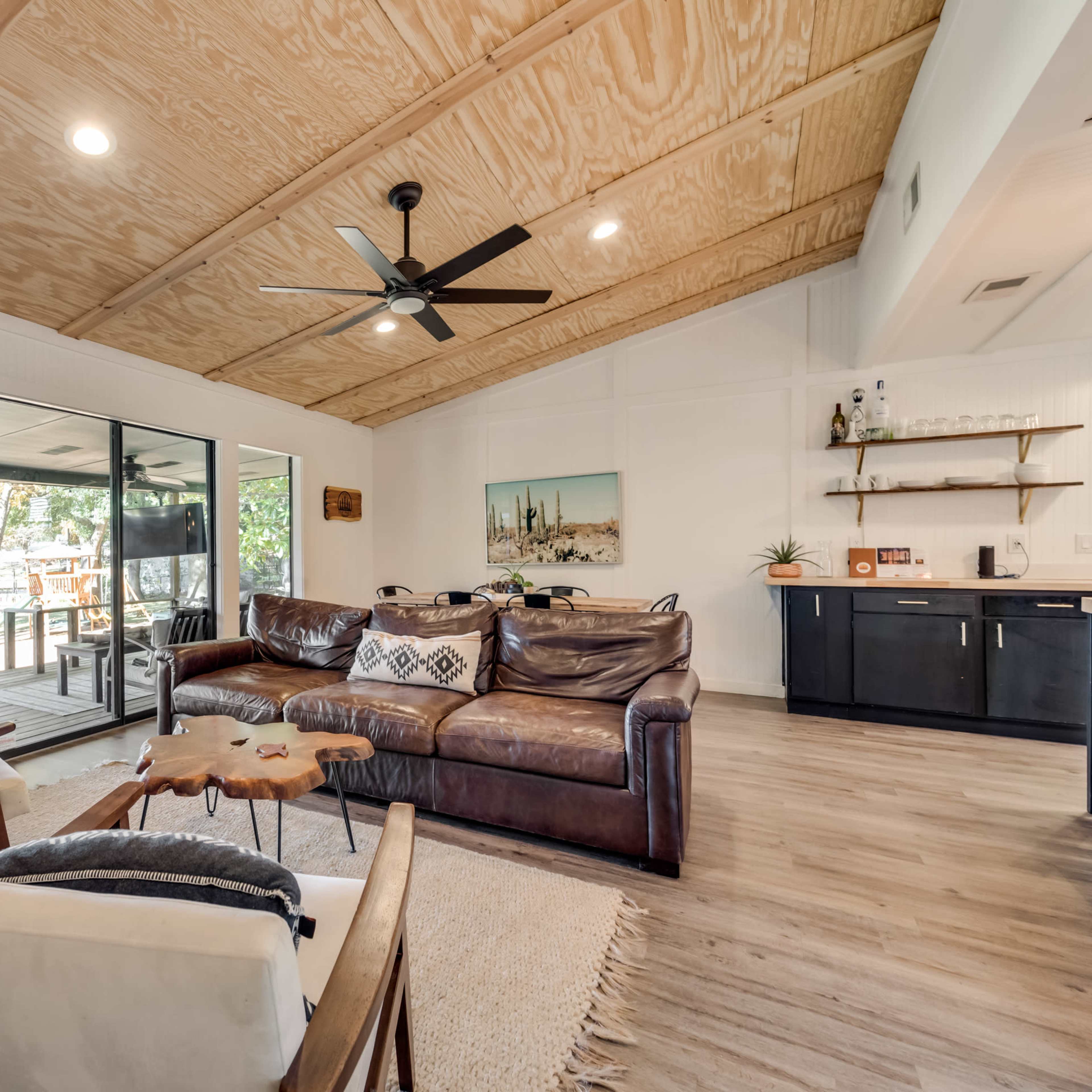 The living room features a leather sectional sofa, a wooden coffee table, and large sliding glass doors that lead to an outdoor deck.