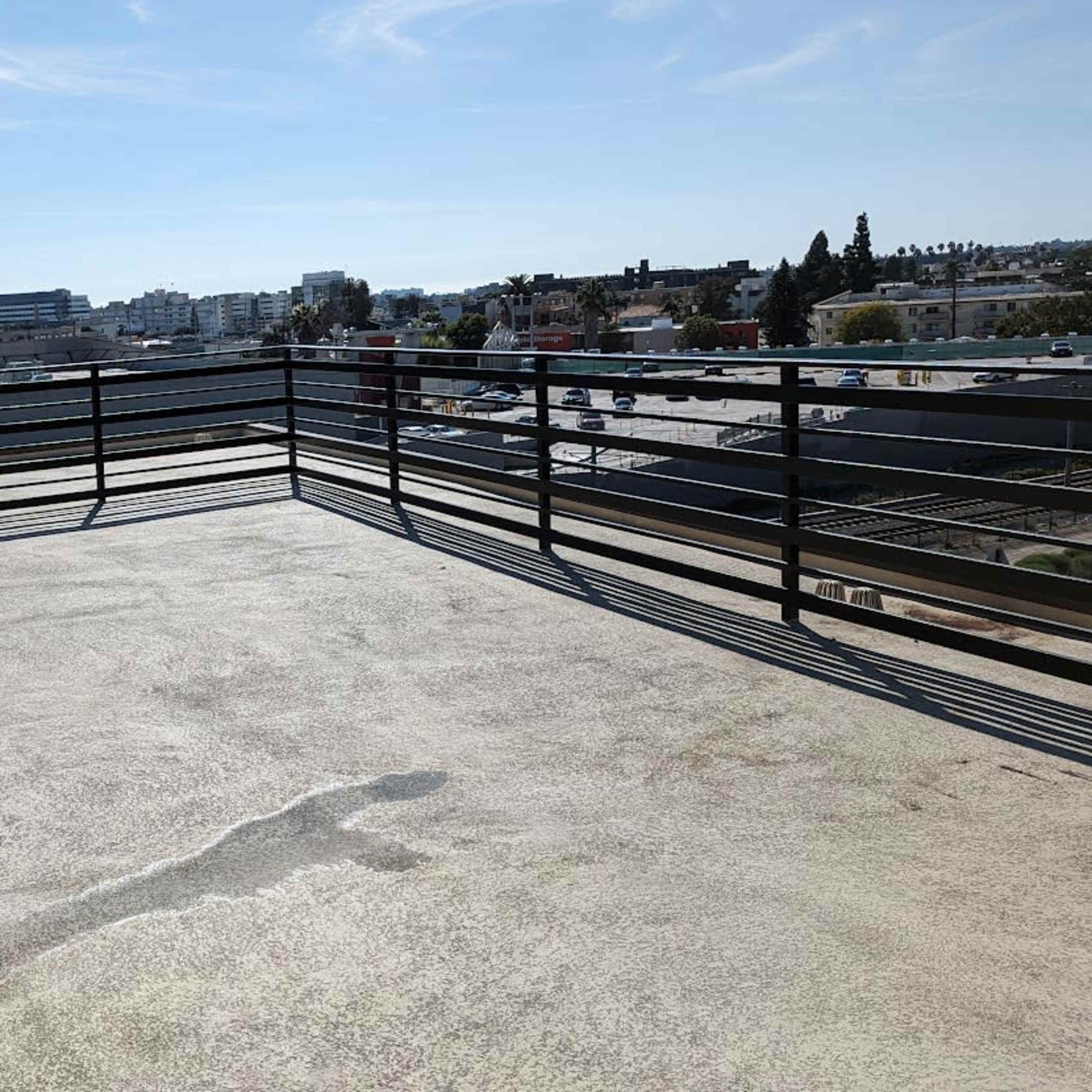 A spacious balcony with a clear view of buildings and a highway in the background under a bright blue sky.