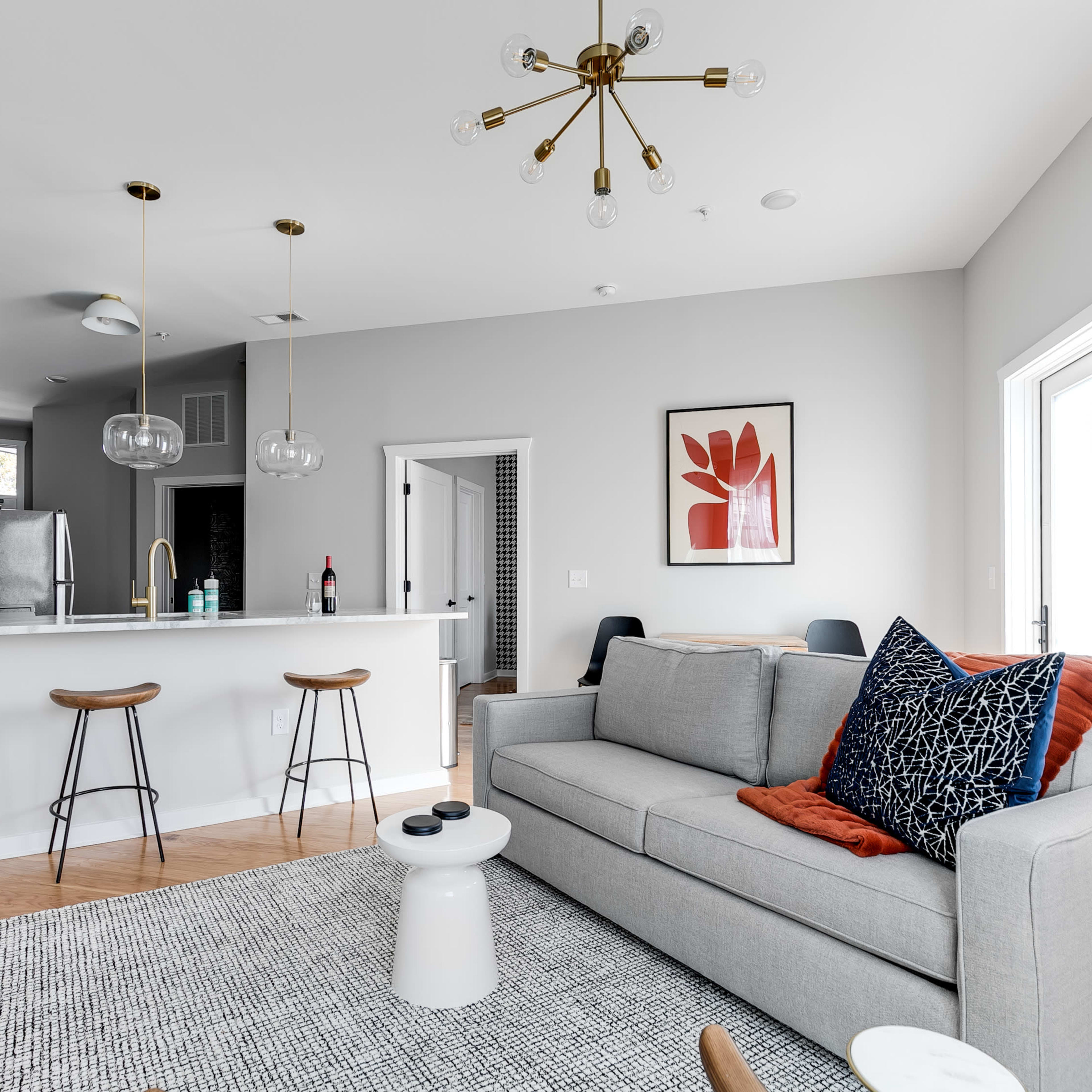 A modern living room featuring a gray sofa, a round coffee table, a wall-mounted television, and a kitchen area with a bar counter.
