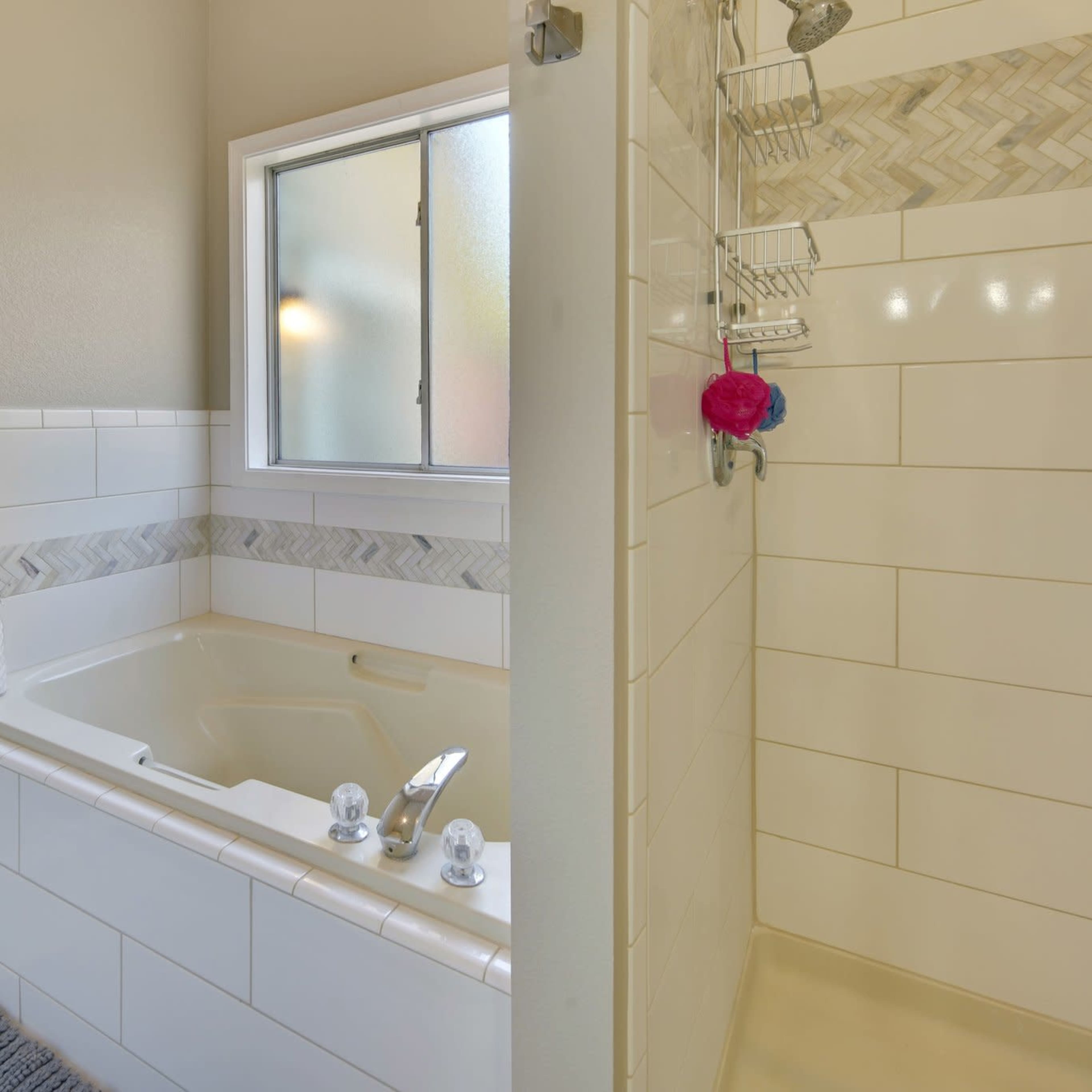 A bathroom featuring a jetted tub beside a glass-enclosed shower, with light-colored walls and a tiled backsplash.