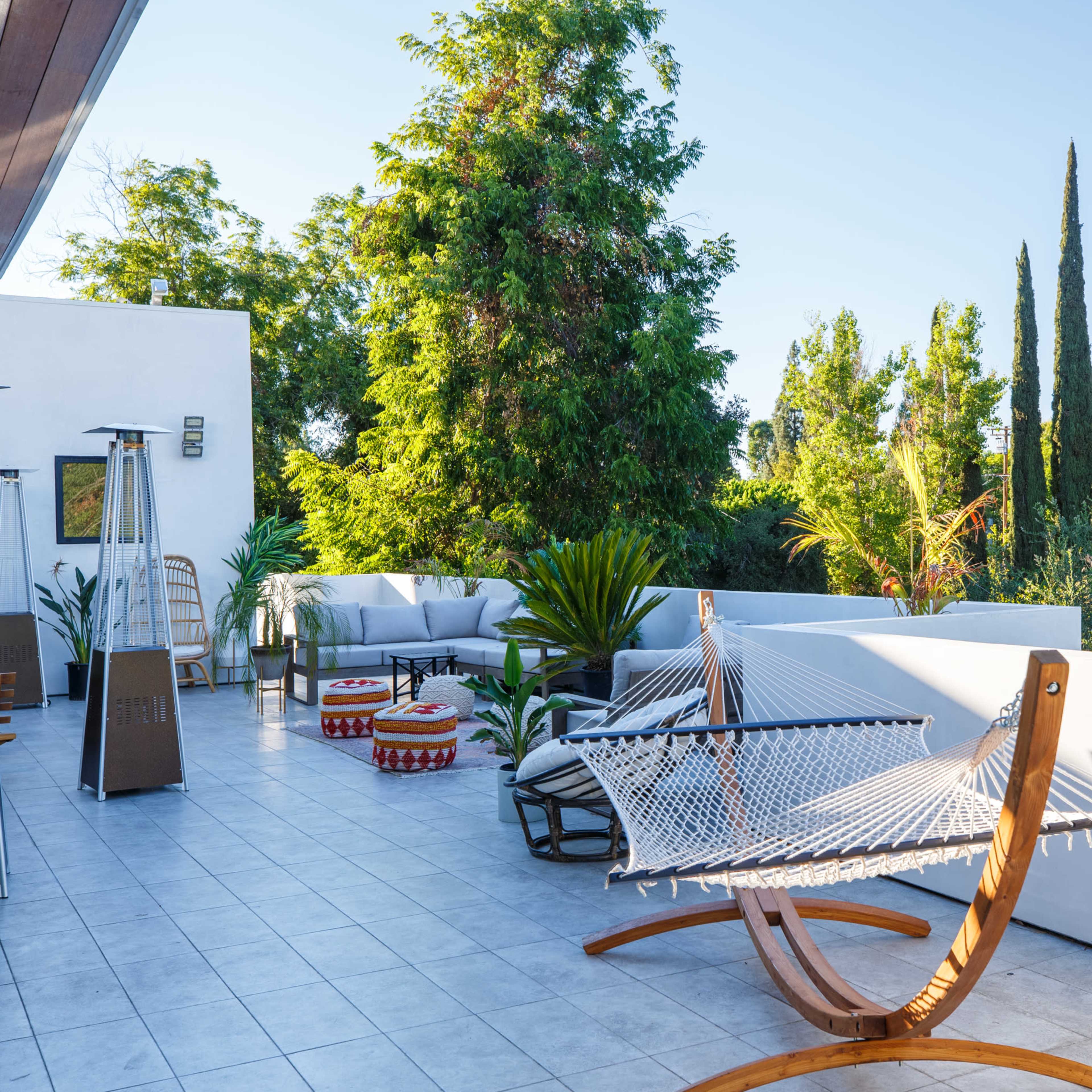 The scene features a spacious outdoor terrace with hammocks, lounge seating, and various potted plants surrounded by greenery.
