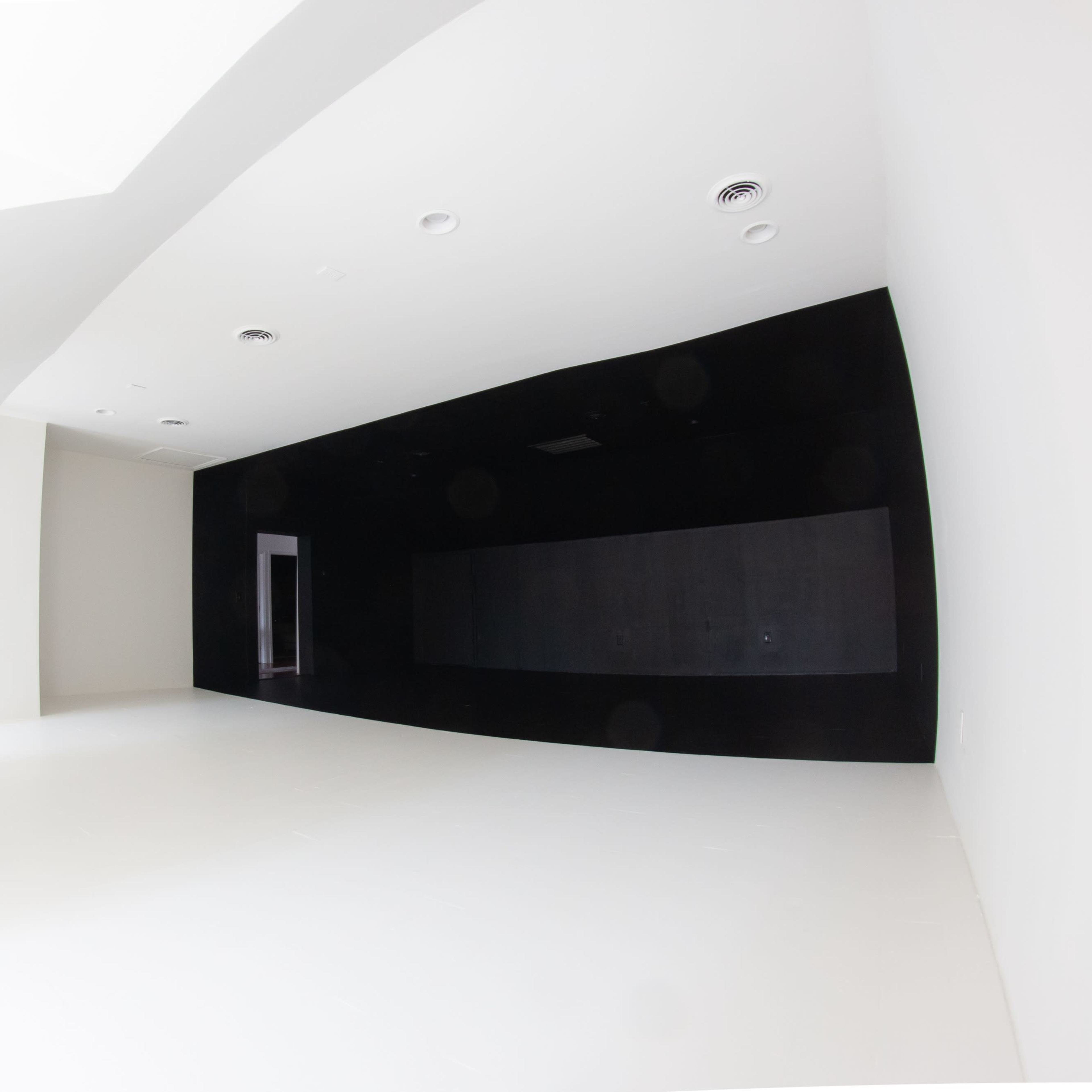 A spacious room with a stark white floor and walls, contrasting with a dark black wall on one side.