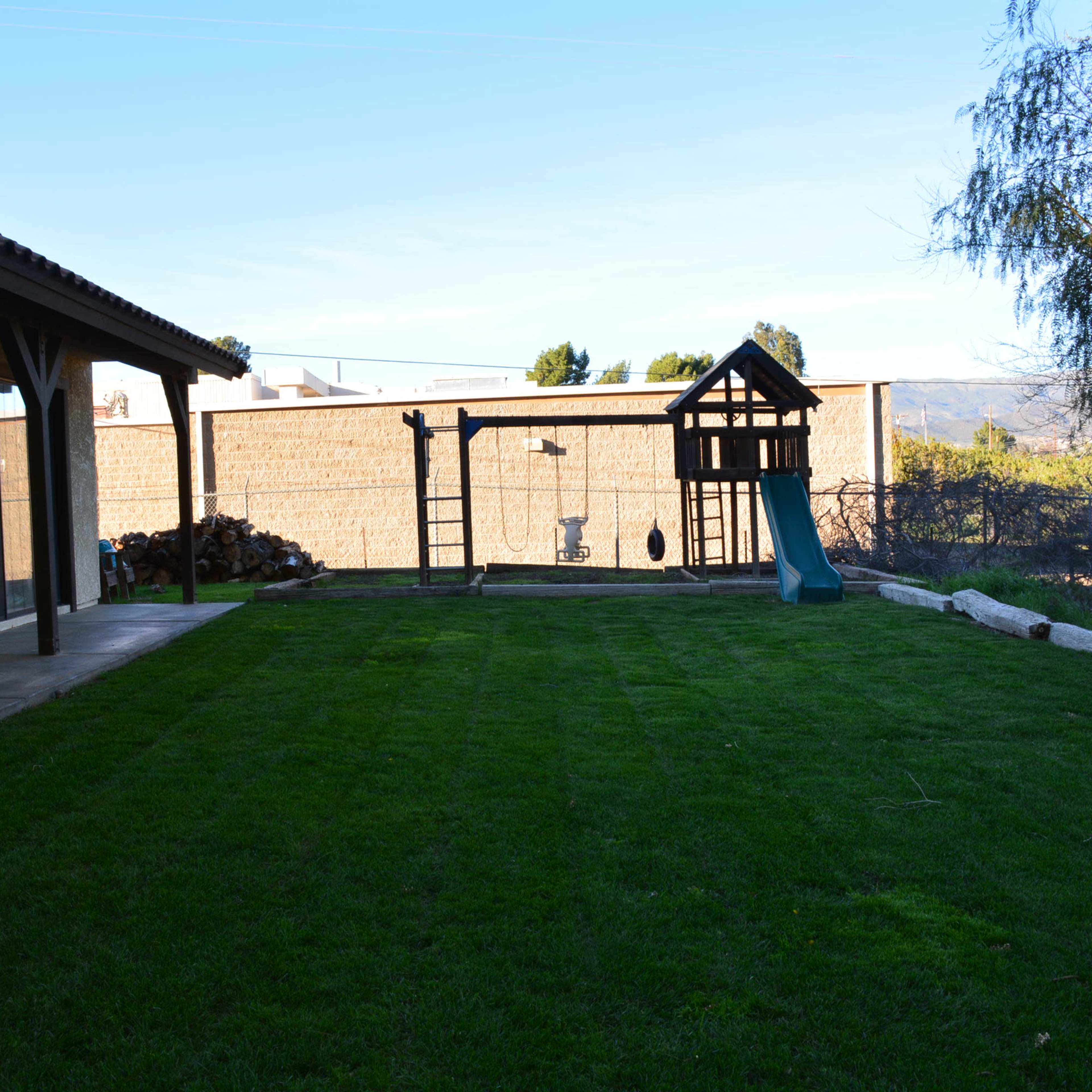 A backyard with a neatly maintained lawn, a playset, and a clear sky in the background.