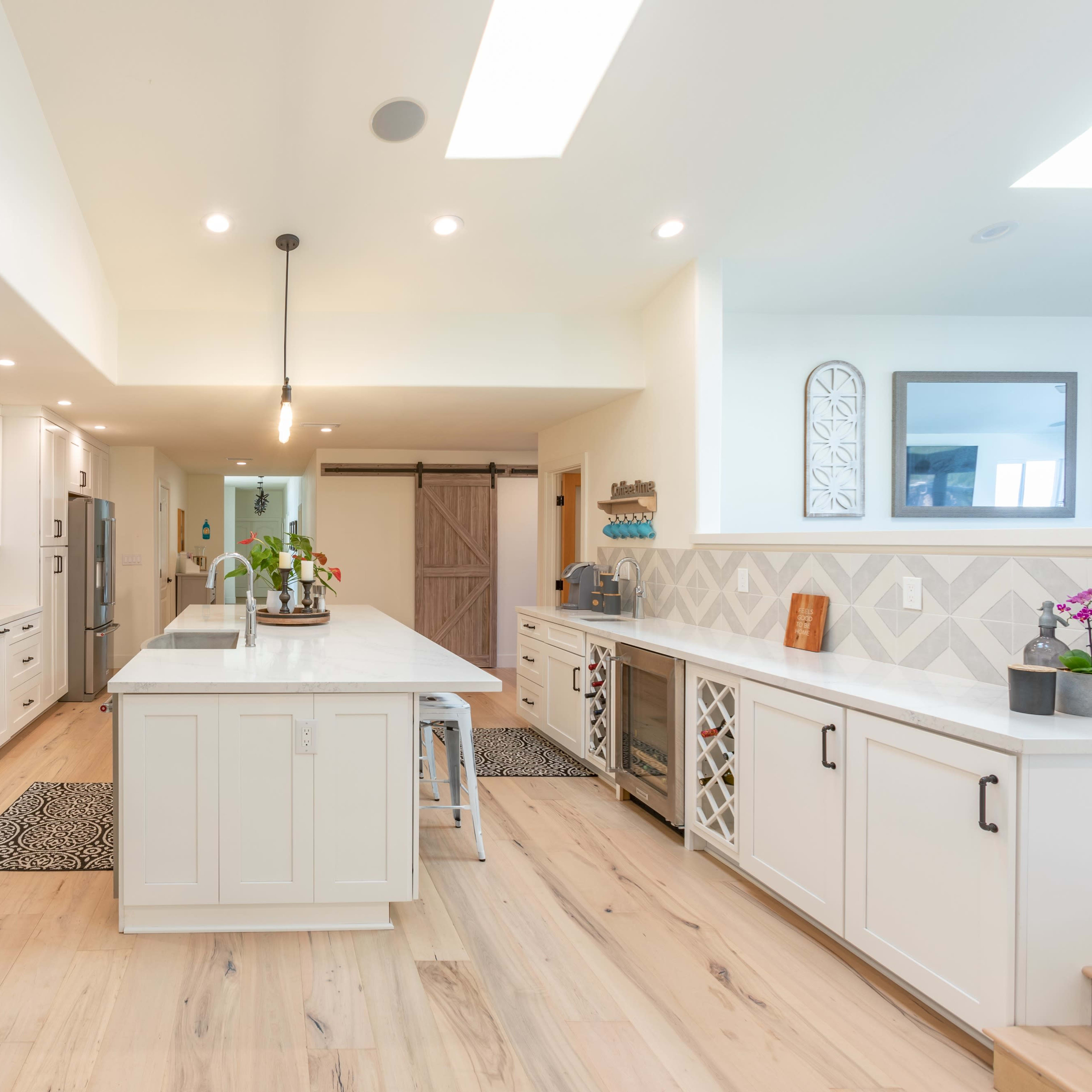 A modern kitchen features white cabinets, stainless steel appliances, and a large central island with pendant lighting.
