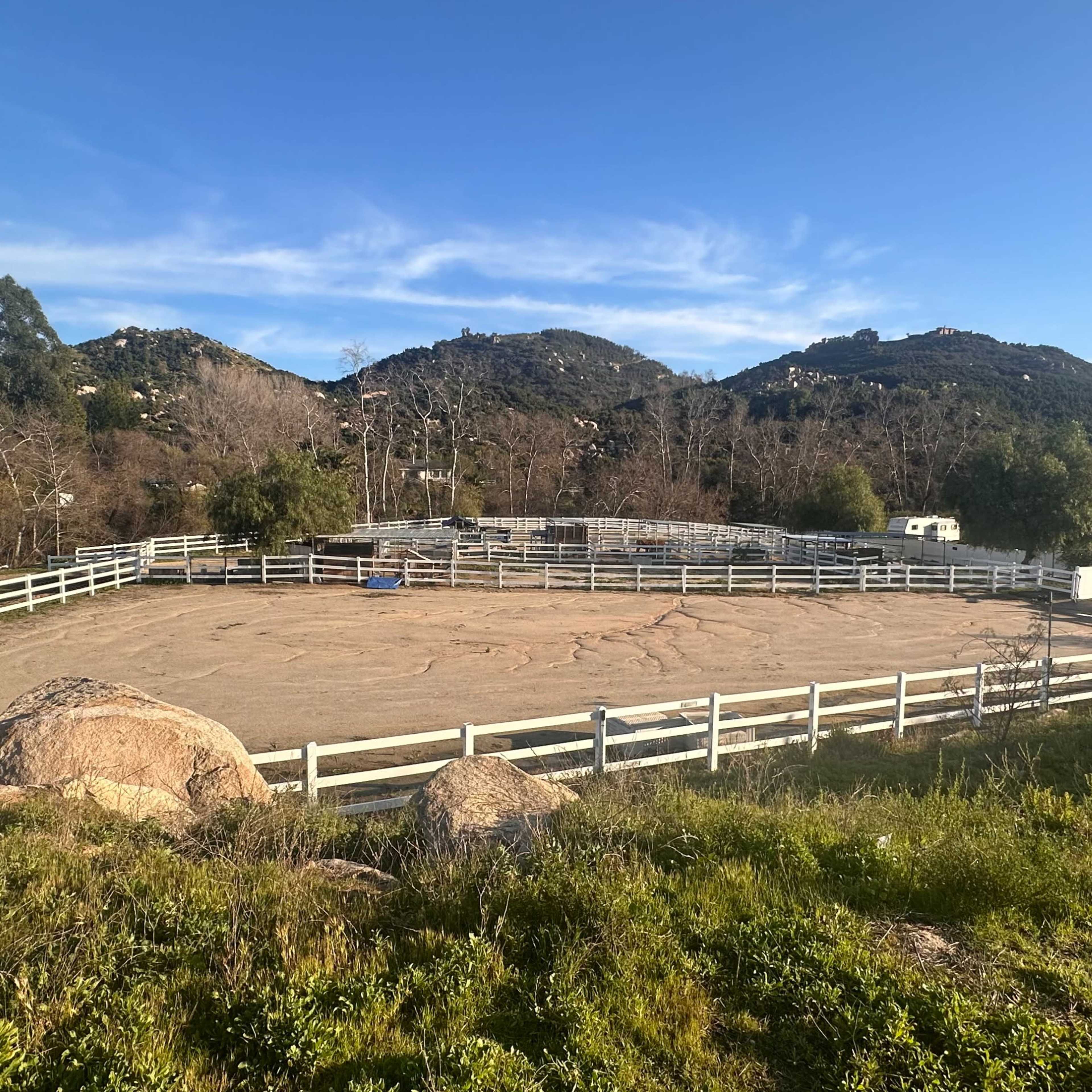 A fenced riding arena surrounded by hills and sparse vegetation.