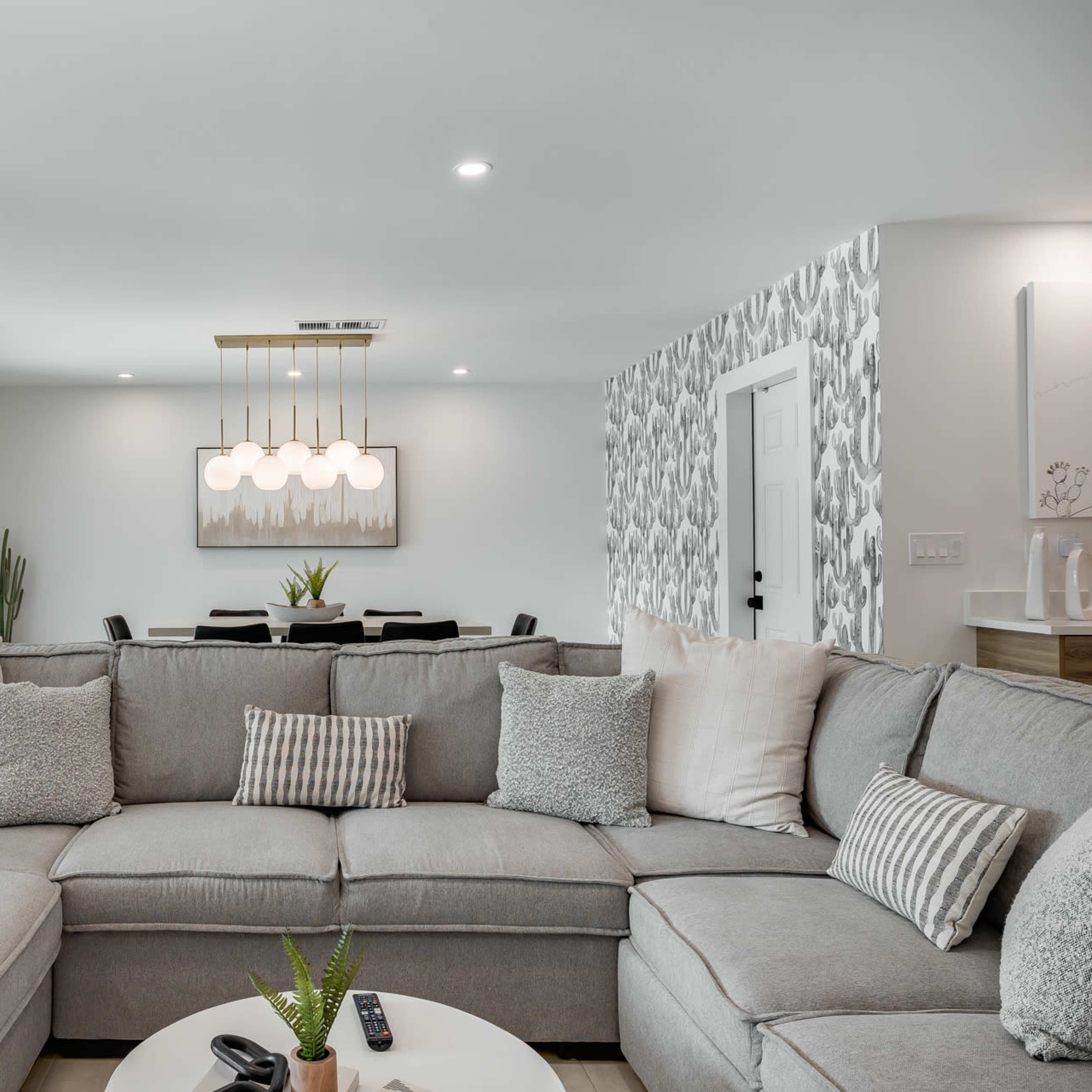 A modern living room featuring a large gray sectional sofa with decorative pillows, a coffee table, and framed artwork on the walls.