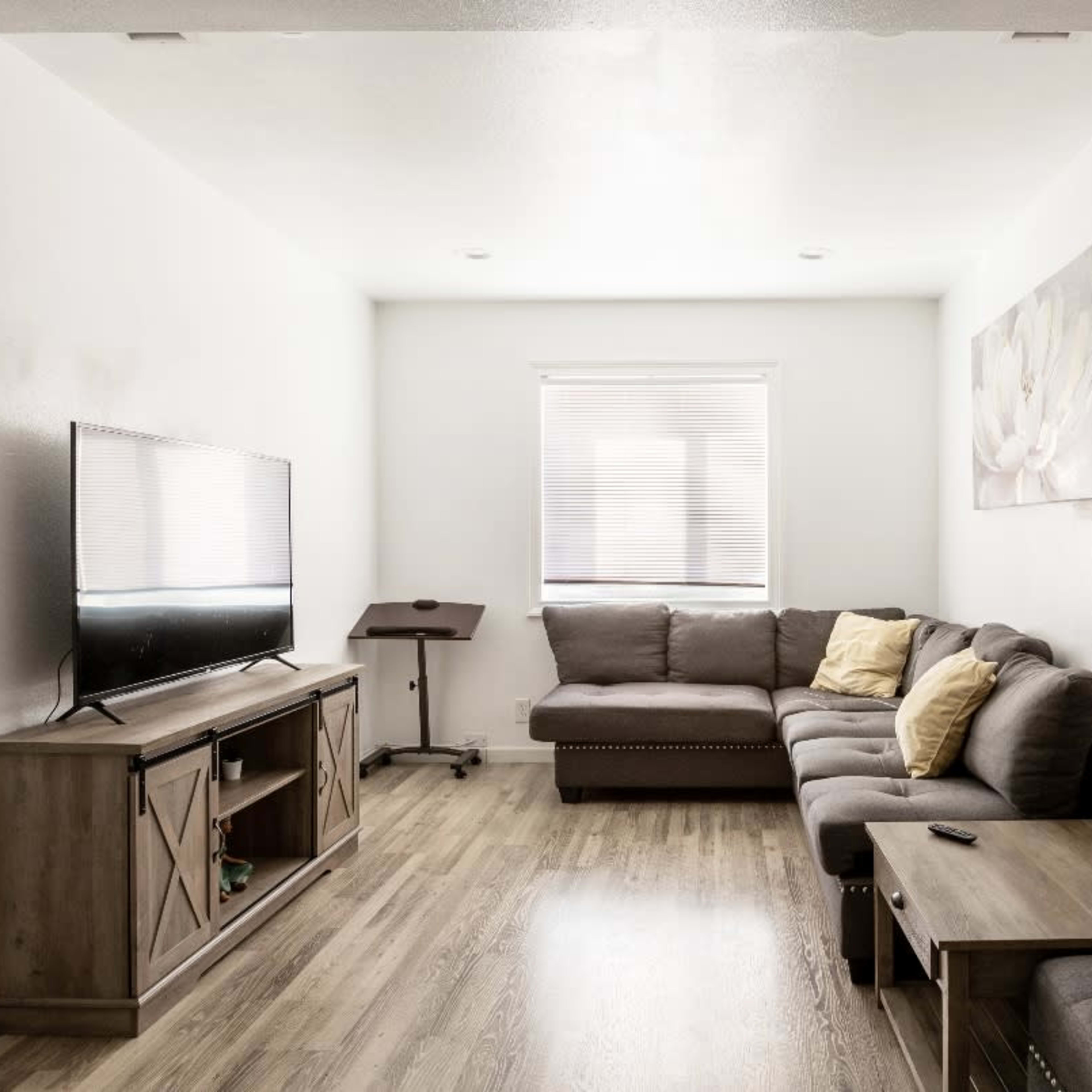 The living room features a sectional sofa, a wooden TV stand, and a small writing desk beside a wall-mounted television.