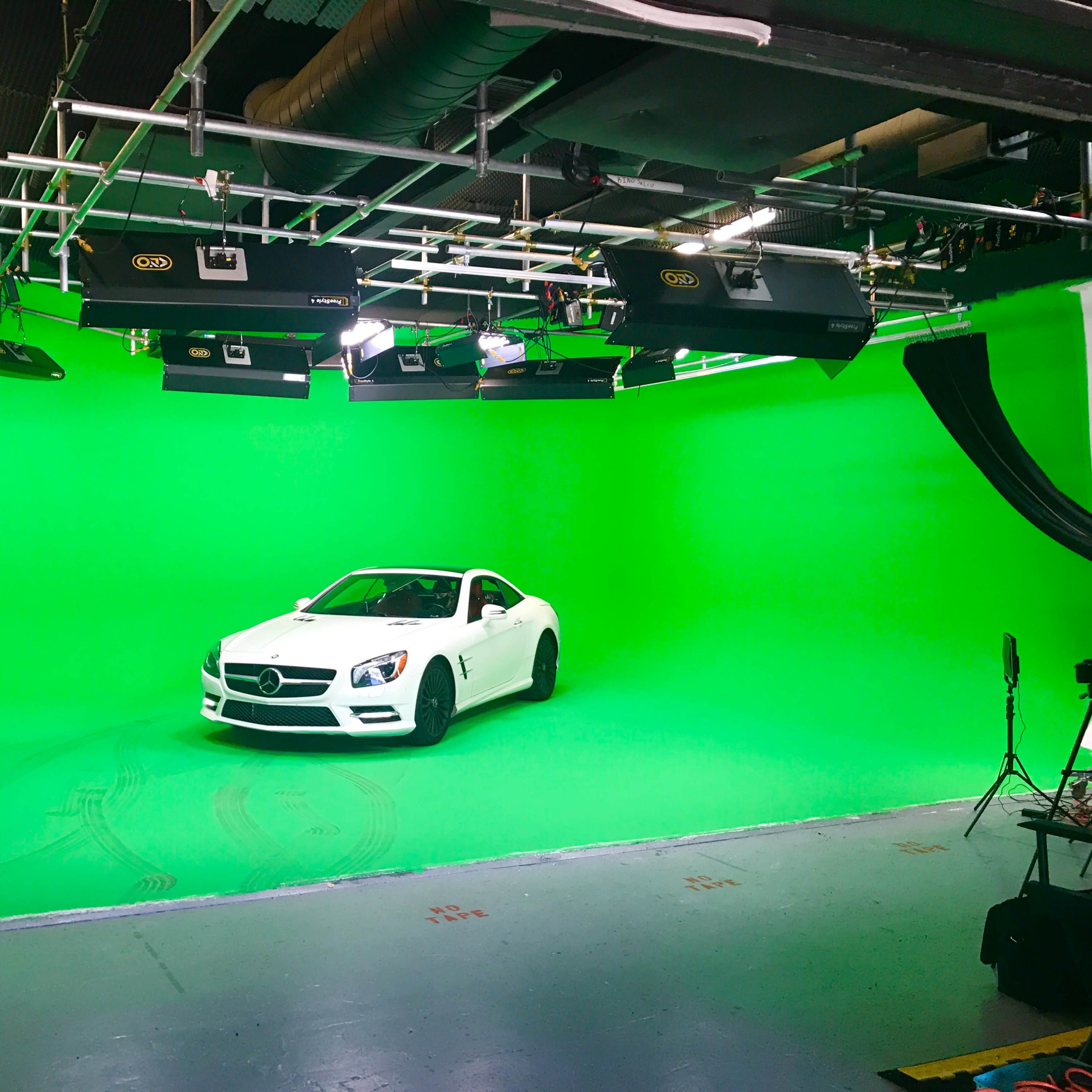 A white convertible car is parked in a studio with a green screen backdrop.
