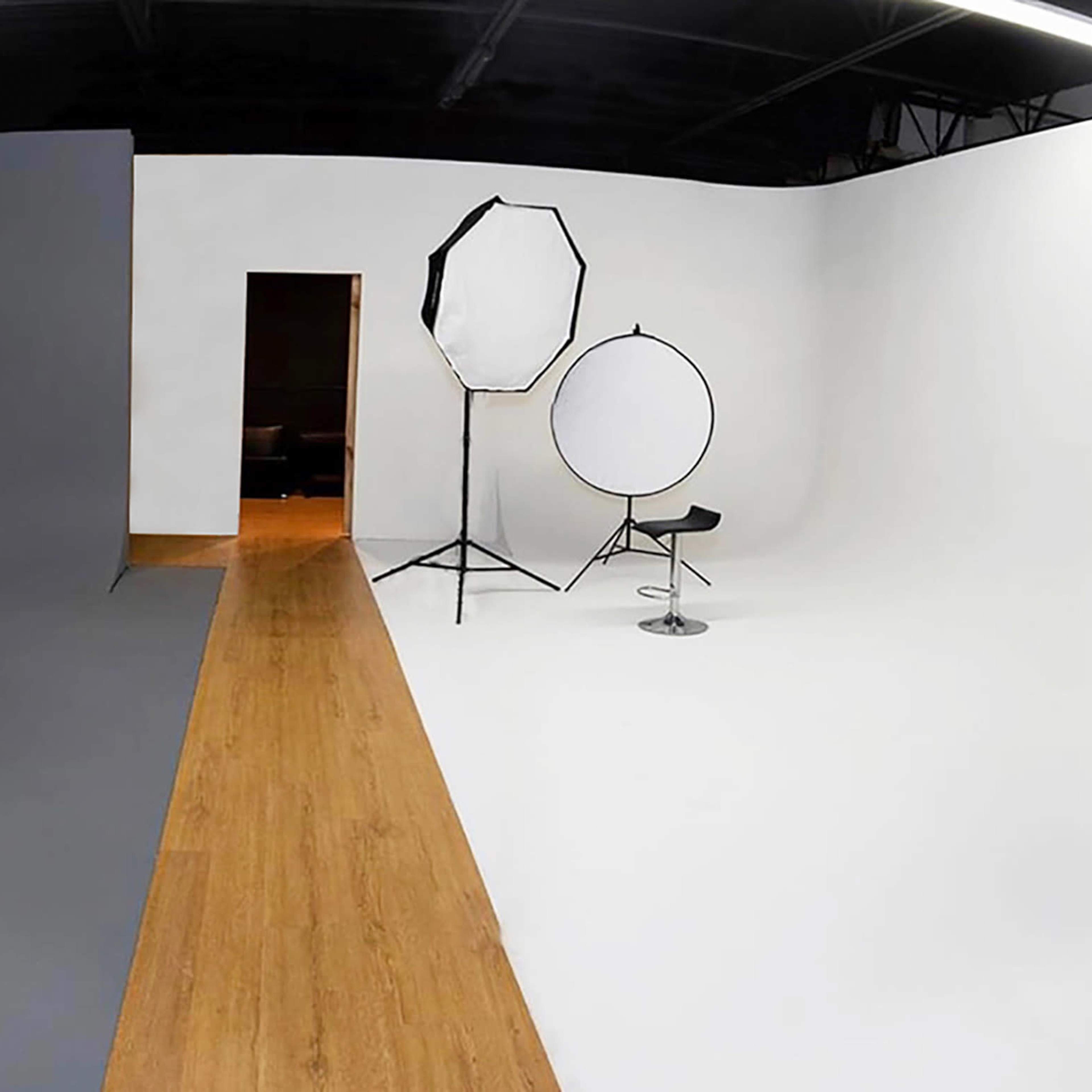 A photography studio with a gray backdrop on one side and a white backdrop on the other, featuring a chair and two lighting setups.