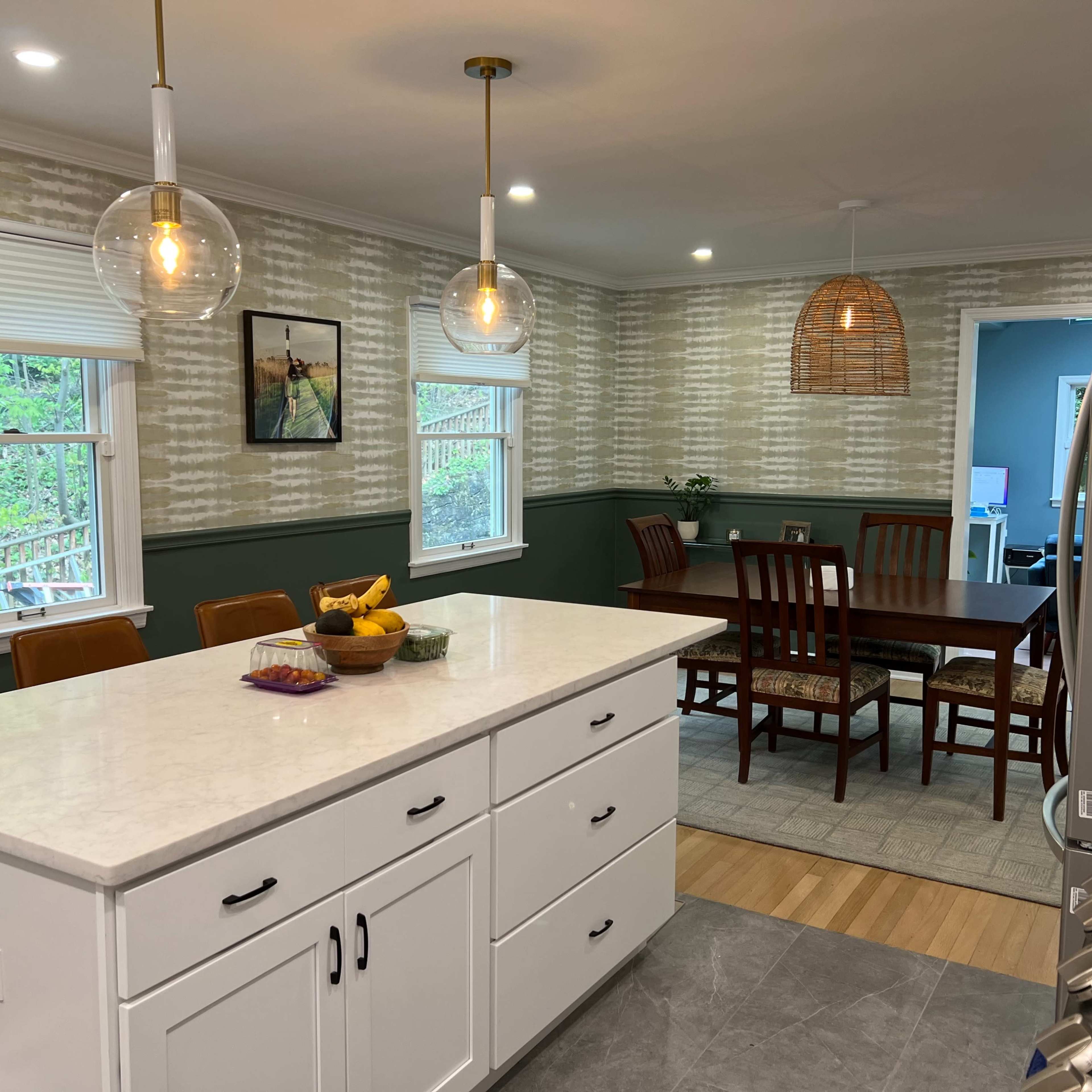 A modern kitchen with a central island, seating for four, and adjoining dining area featuring a wooden table and chairs.