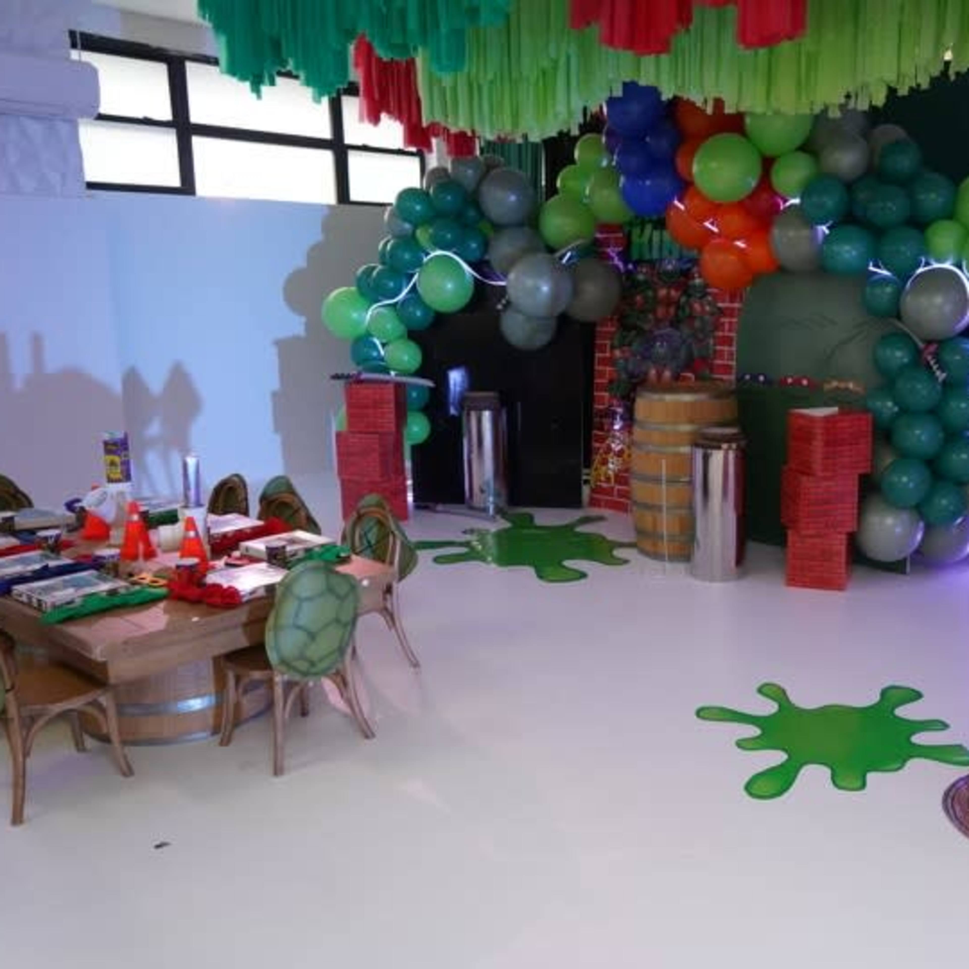 A decorated party space featuring green and colorful balloons, a table set with party supplies, and a splash-themed design on the floor.