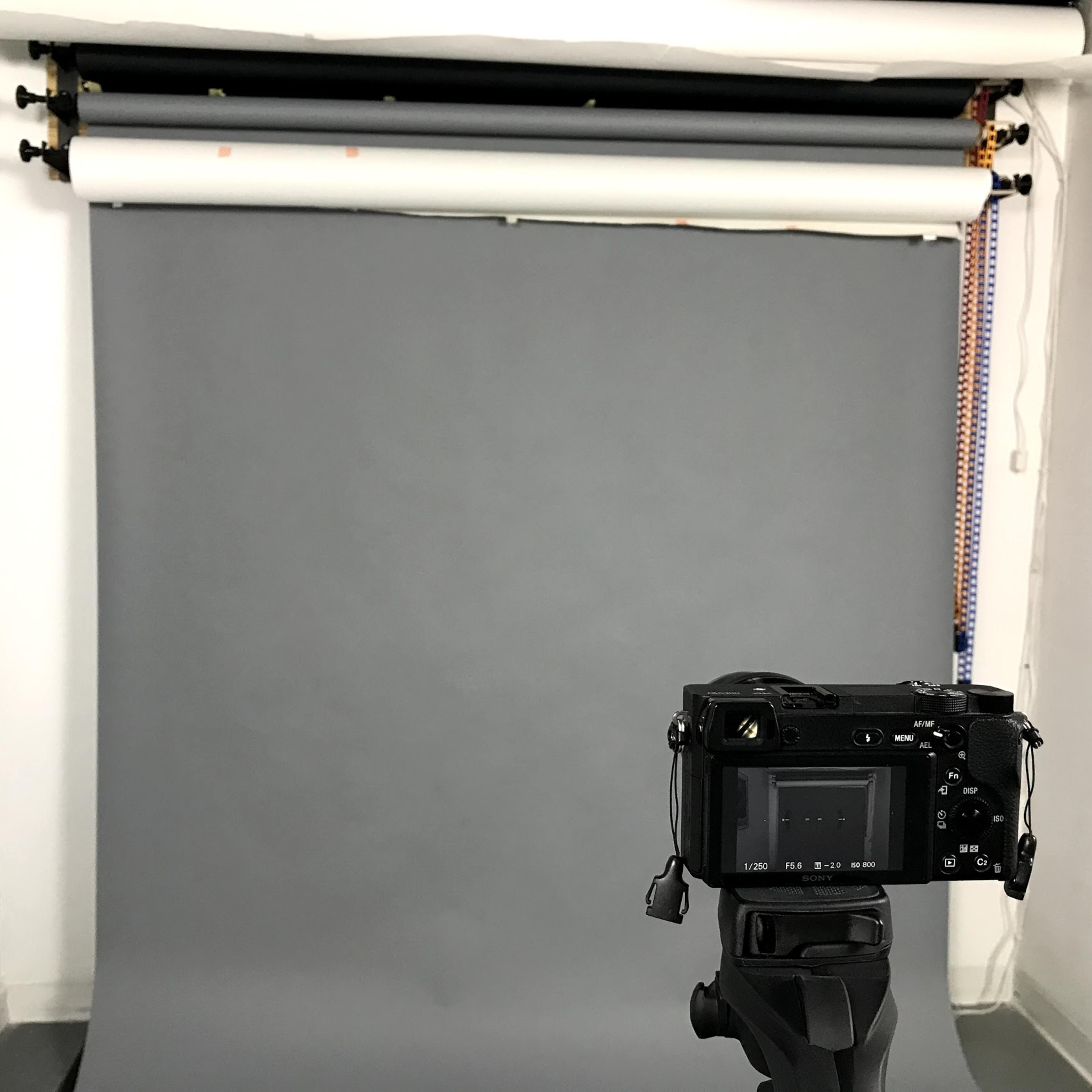 A camera is positioned on a tripod in front of a gray backdrop in a photography studio.