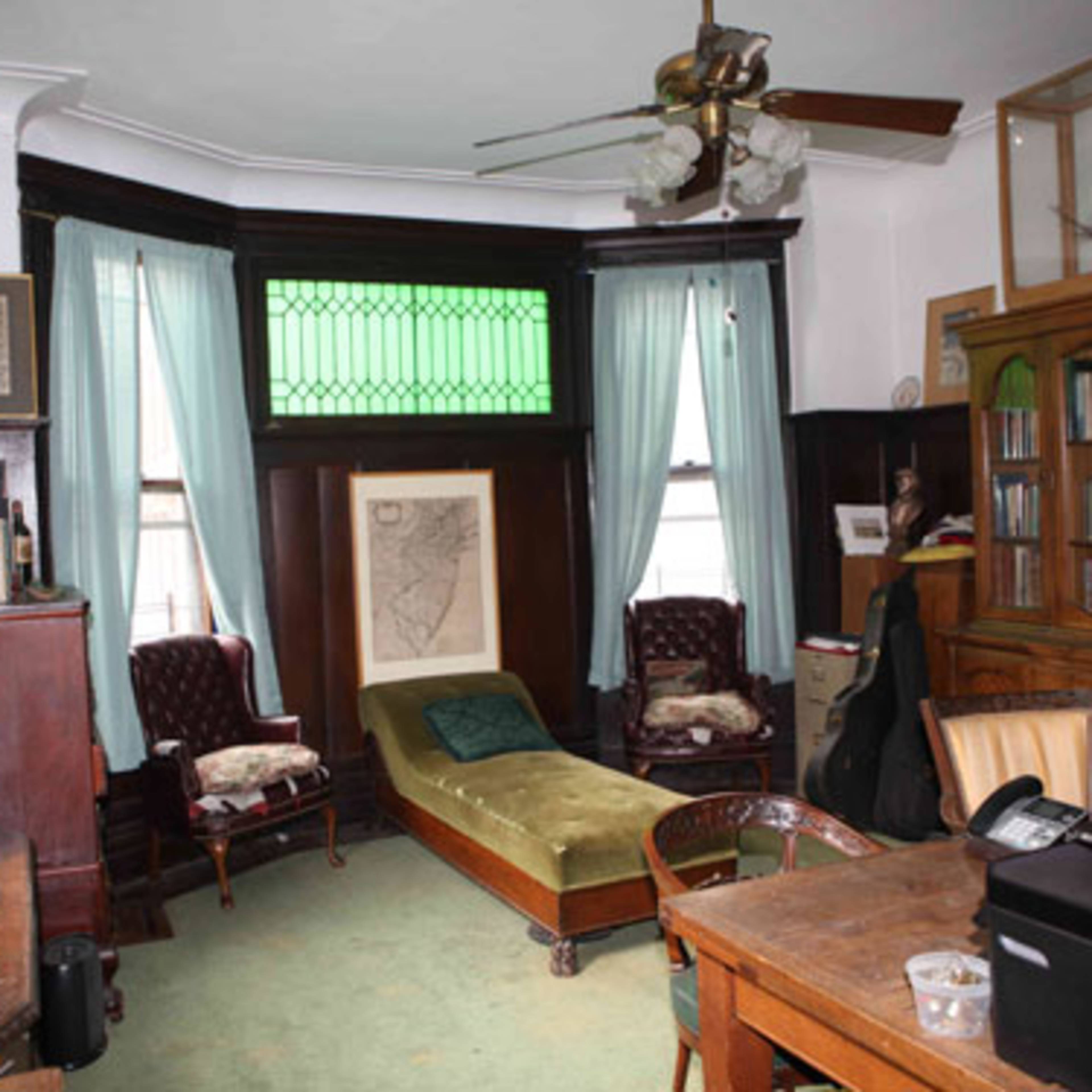 A room with two chairs, a chaise lounge, a wooden bookshelf filled with books, and a desk with a printer.