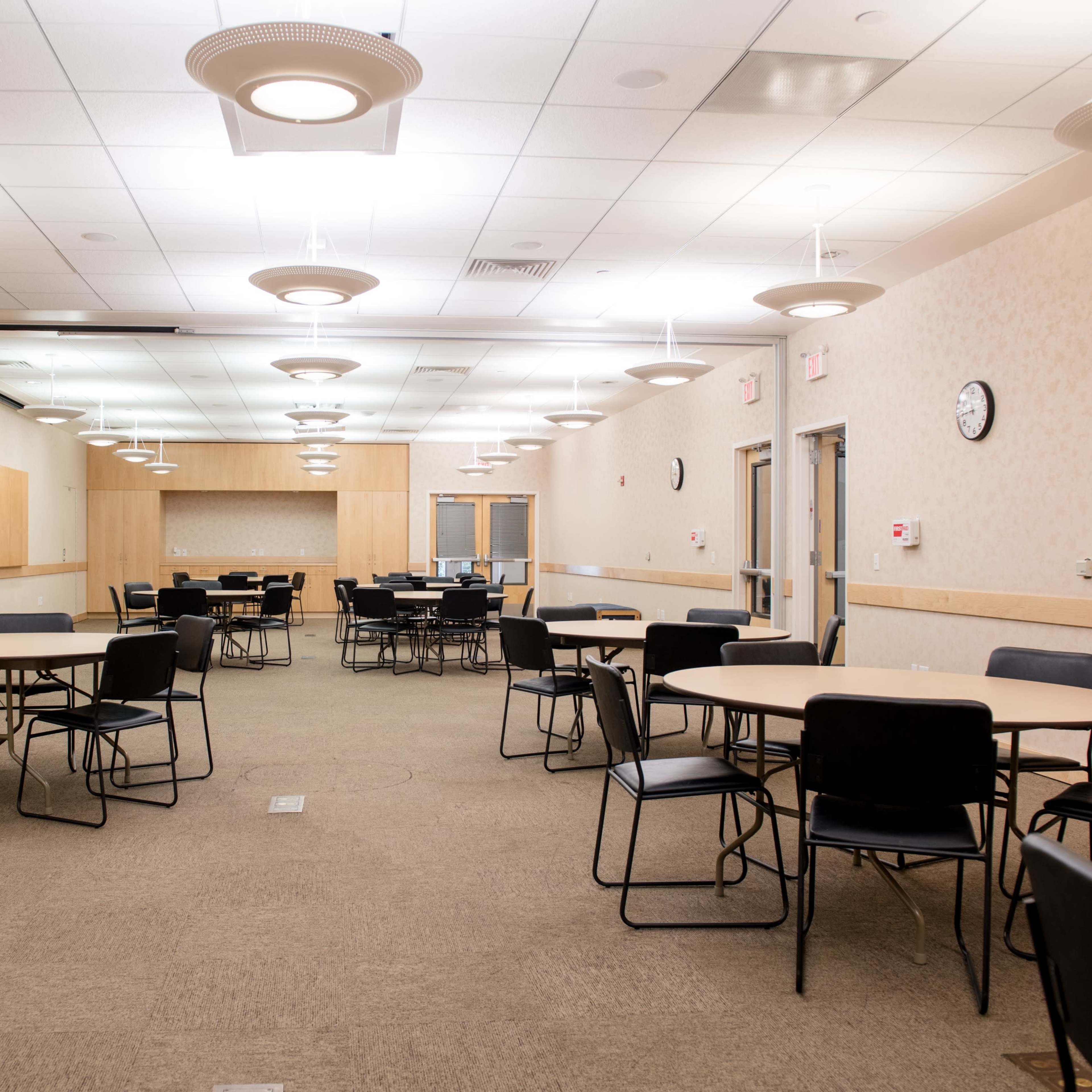 A large, empty meeting room with circular tables and black chairs arranged throughout the space.