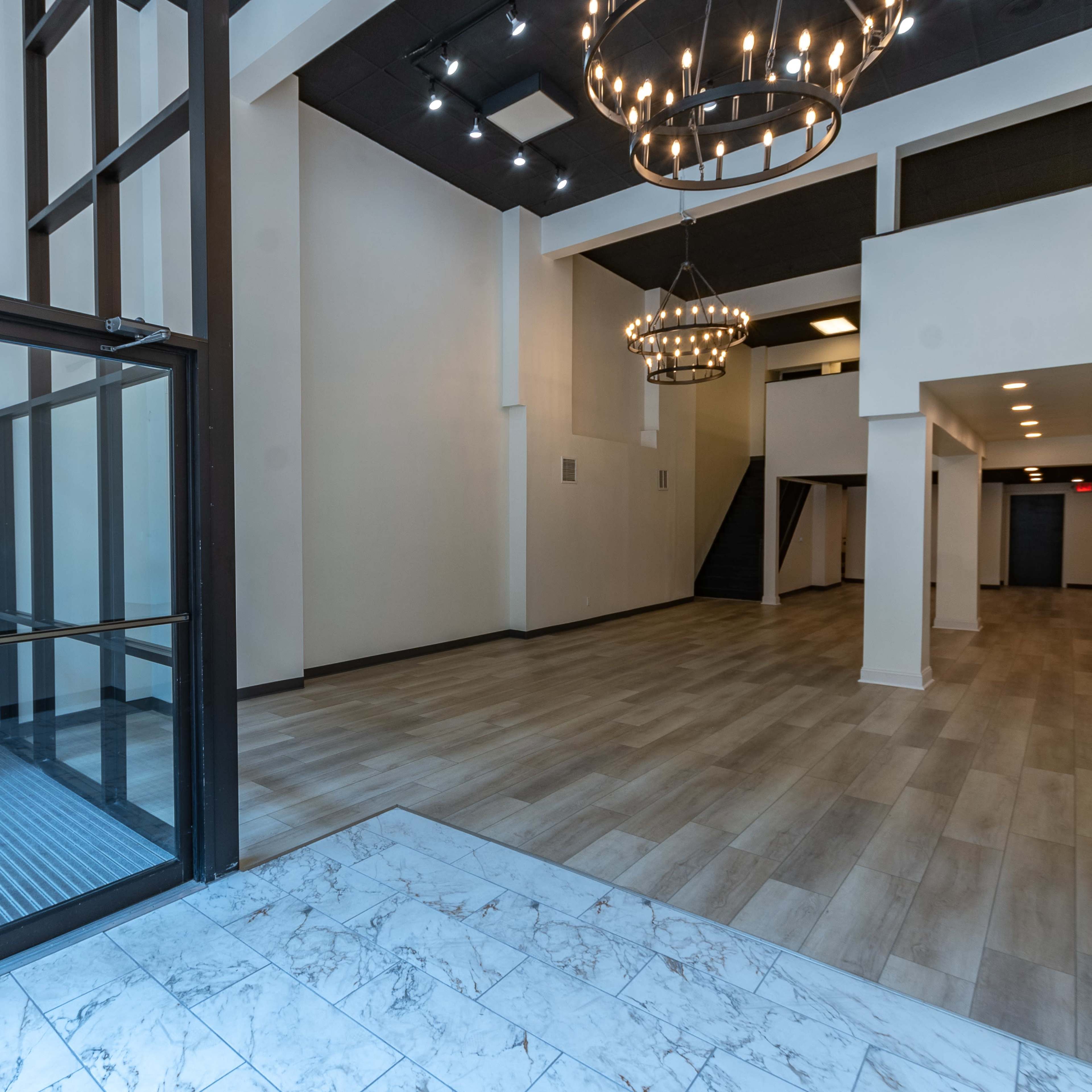 A spacious entryway with a staircase on one side, modern lighting fixtures, and a combination of tile and wood flooring.