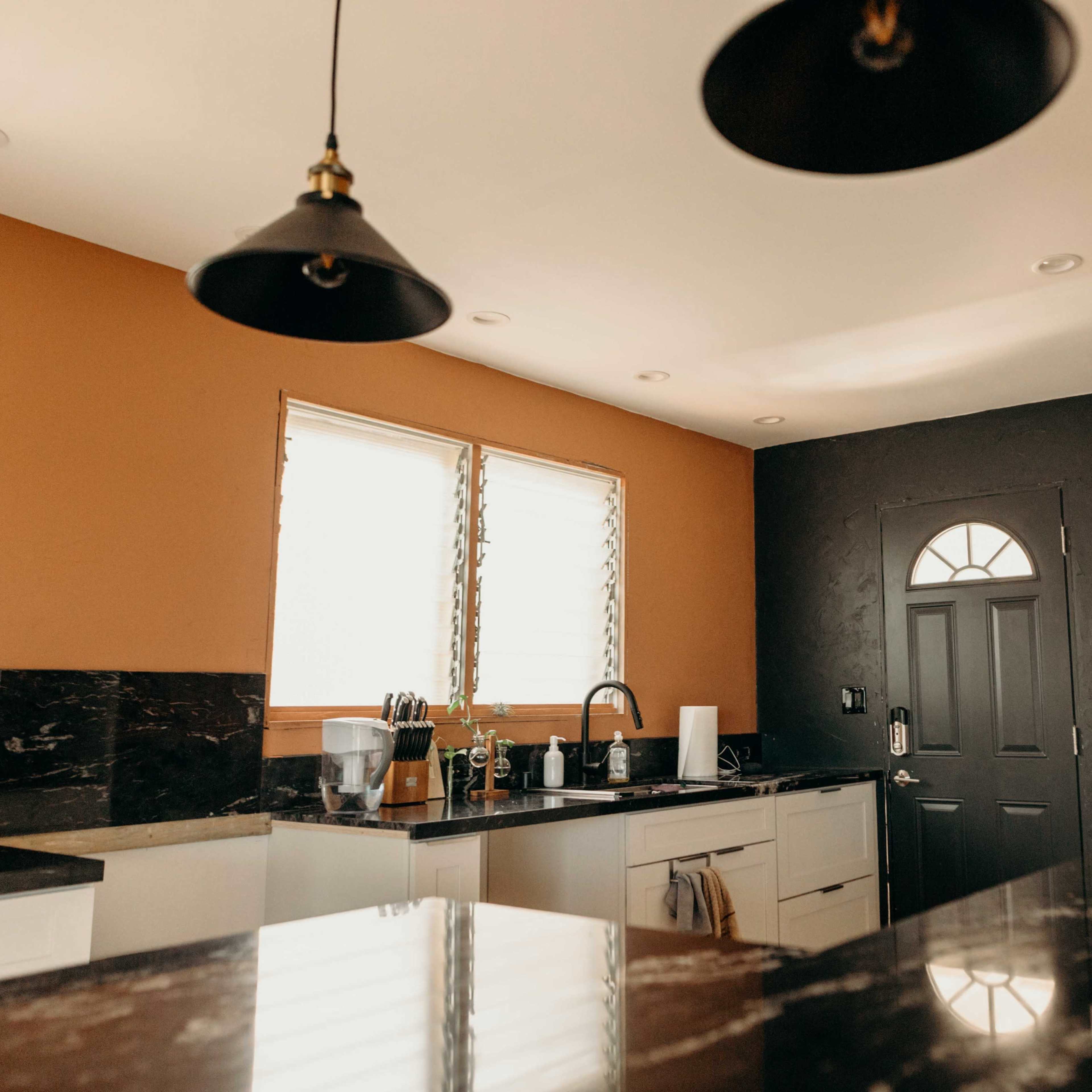 A kitchen with a dark door, large windows, and a mix of light and dark cabinetry.