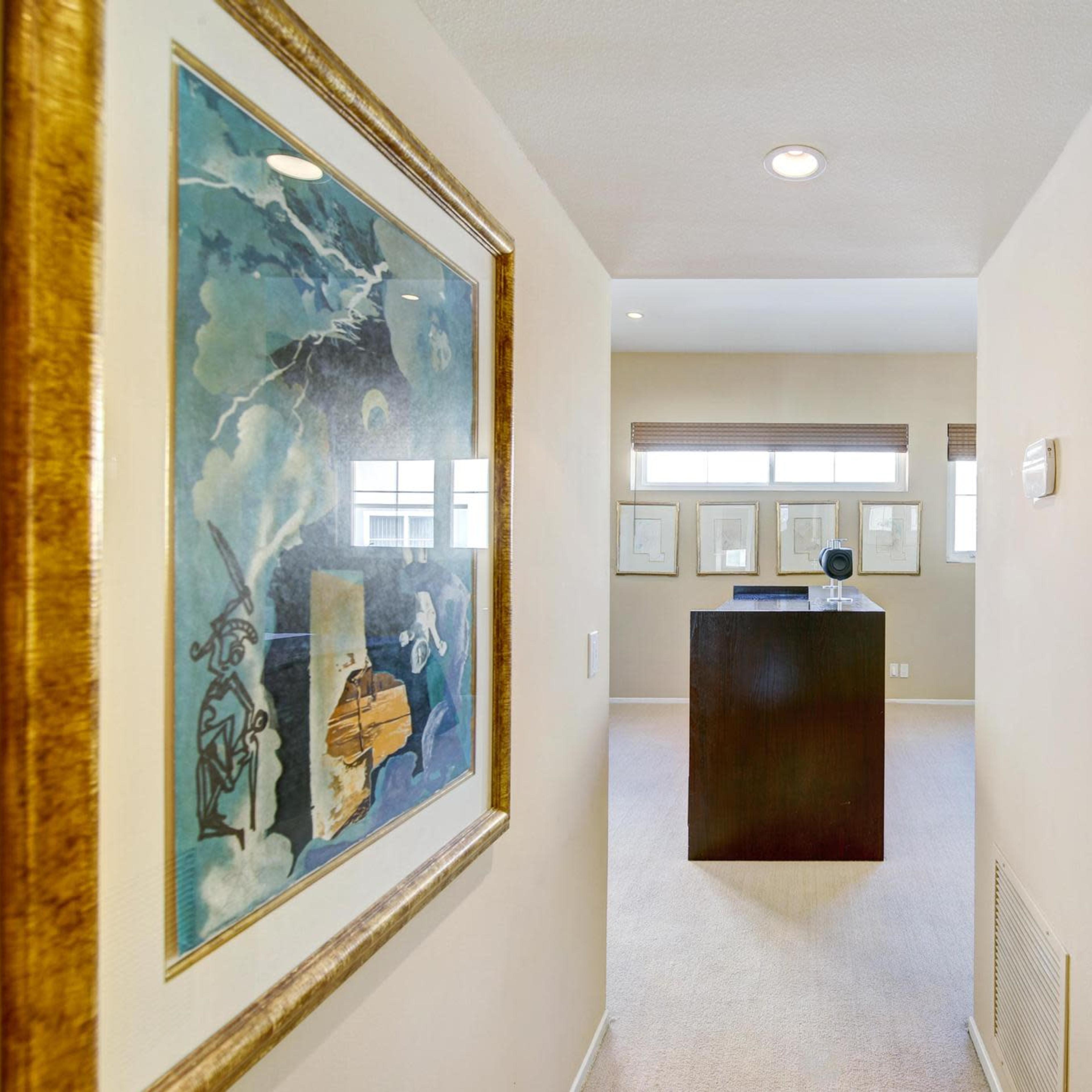 A narrow hallway leads to a room with a dark wooden display and artwork on the walls.