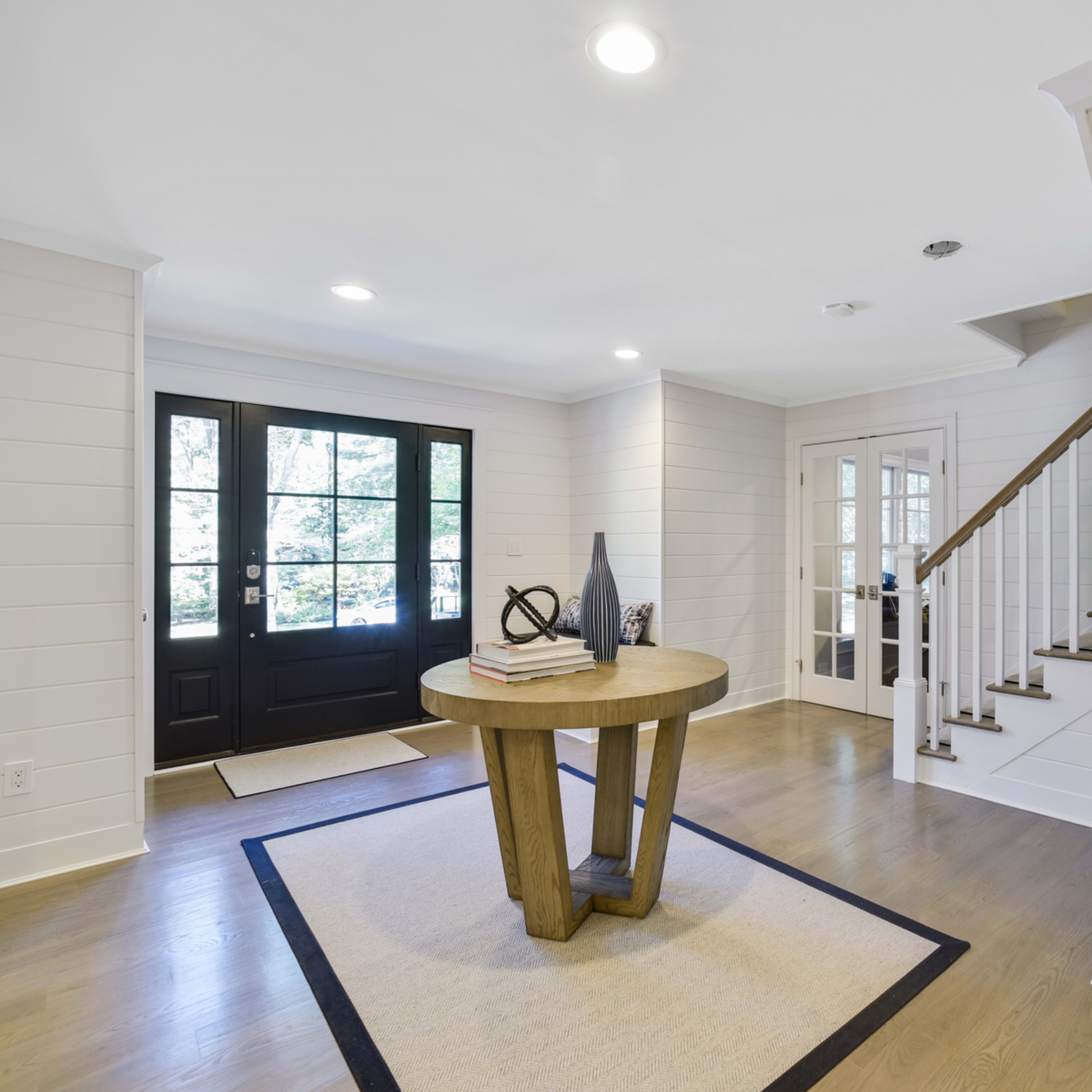 A bright entryway with a round wooden table, a rug, and a staircase leading to an upper level.