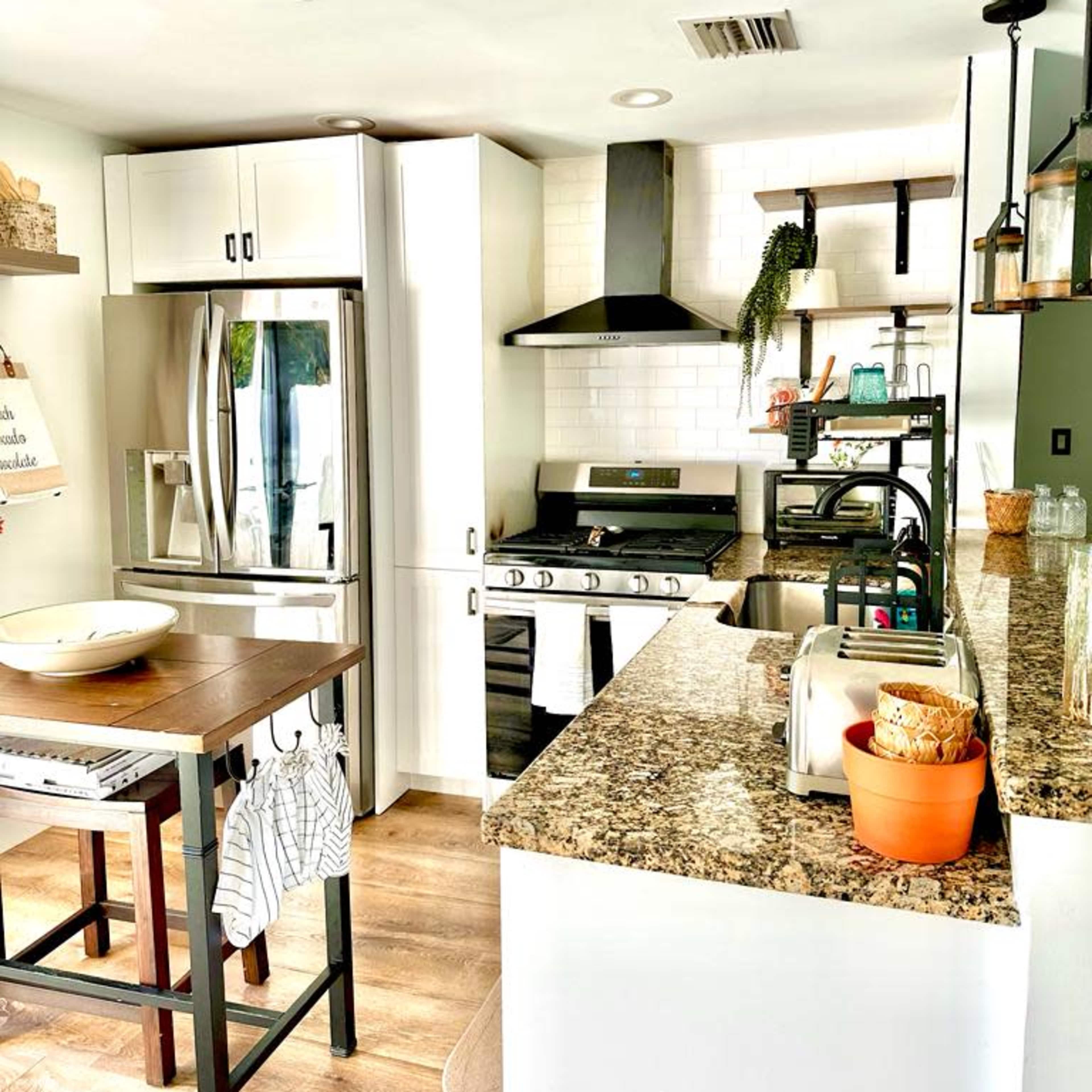 A modern kitchen with white cabinets, a stainless steel refrigerator, a stove, and a wooden dining table.