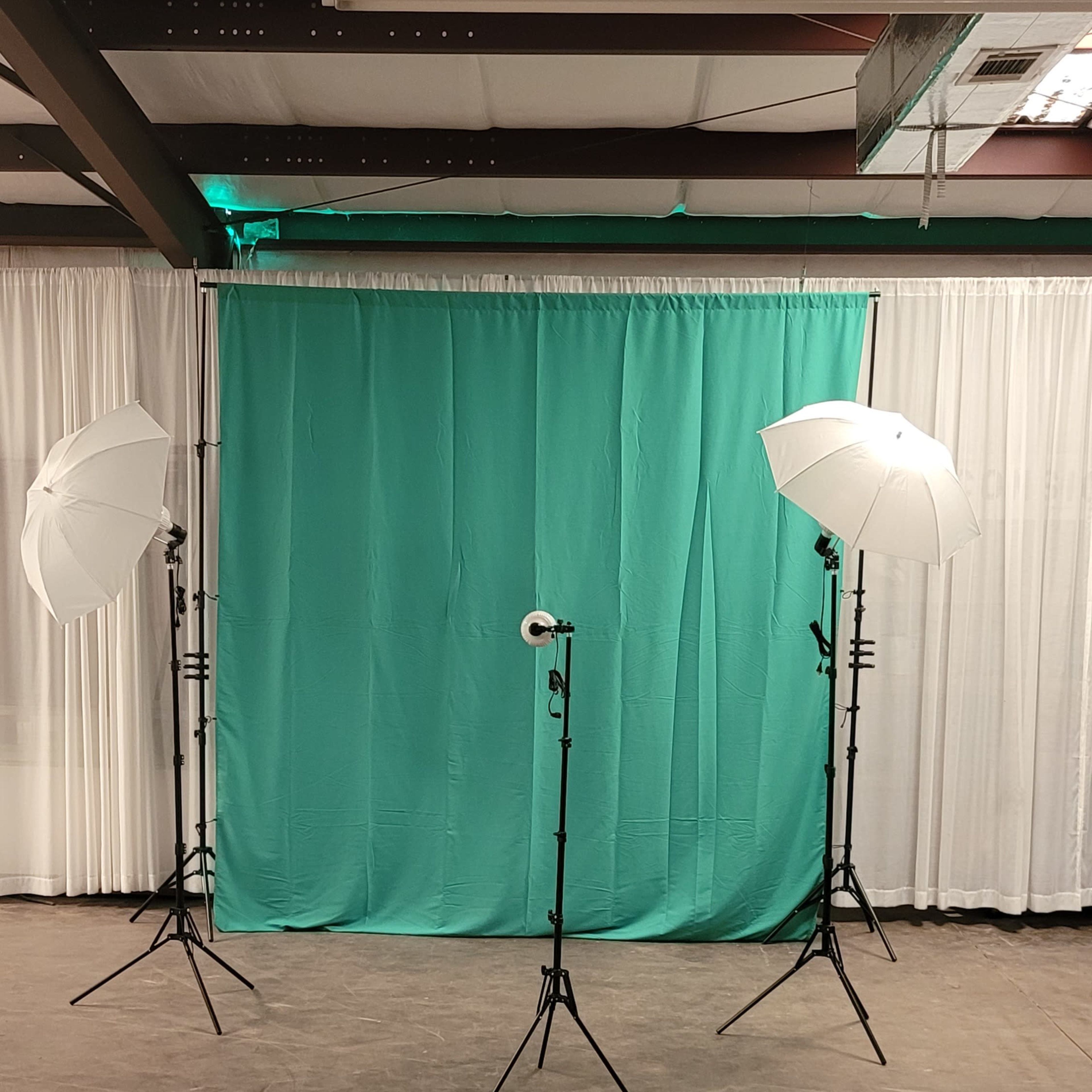 A photography setup with two white umbrella lights and a green backdrop in an empty space.