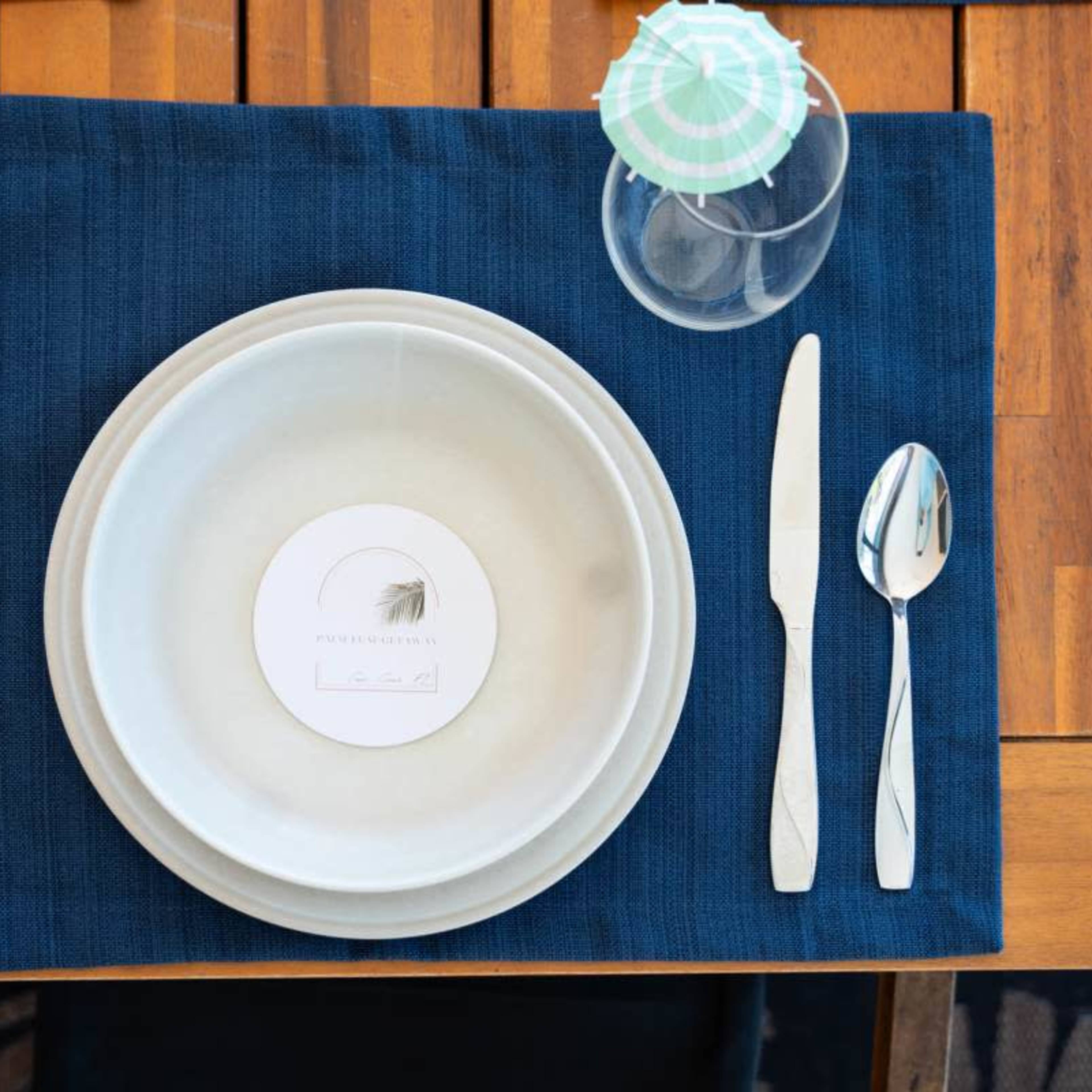 A setting featuring a blue placemat with a circular plate, a menu card labeled "Lead," a fork, knife, and a glass on a wooden table.