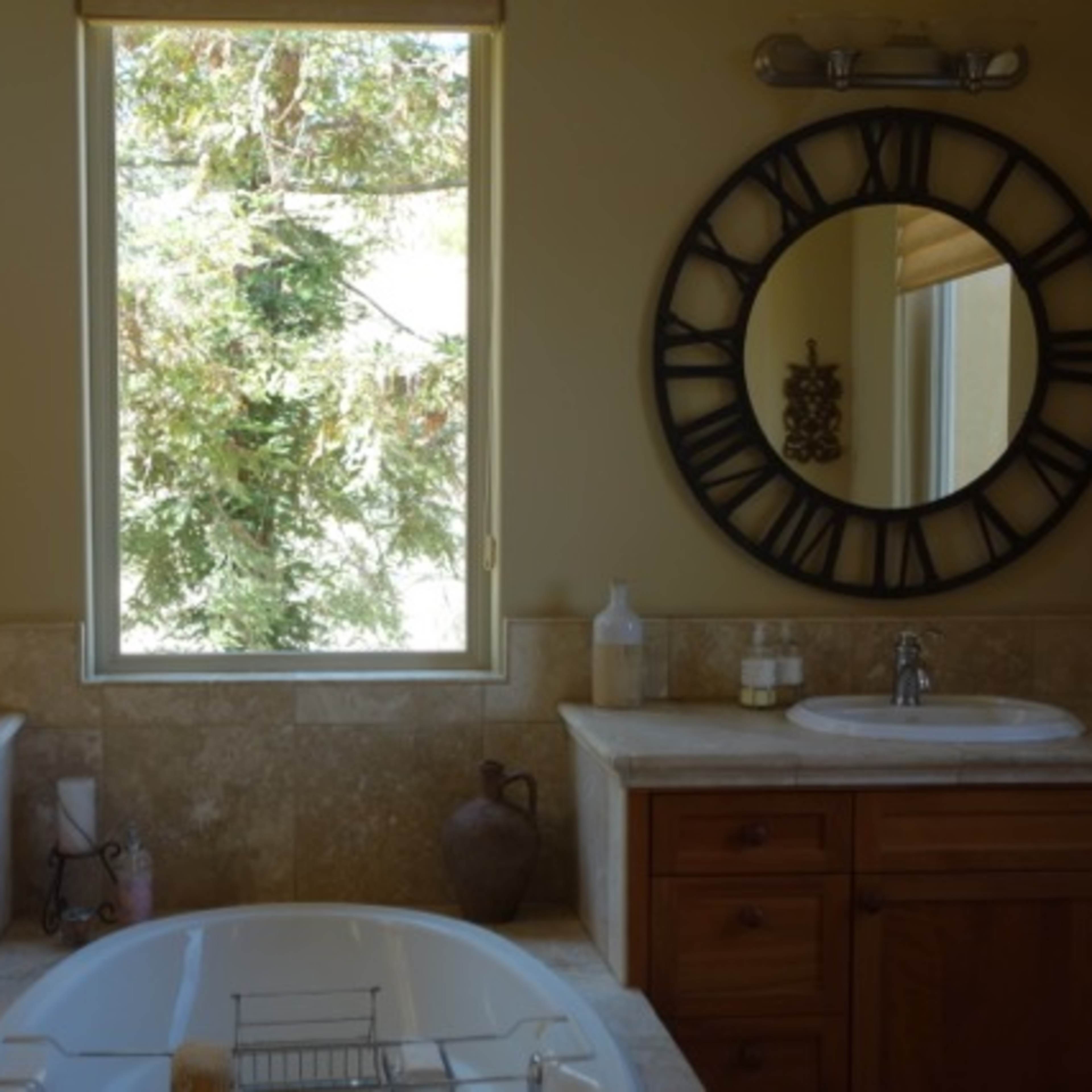 A bathroom with two circular mirrors above separate sinks, a large window providing a view of trees, and a freestanding bathtub in the center.