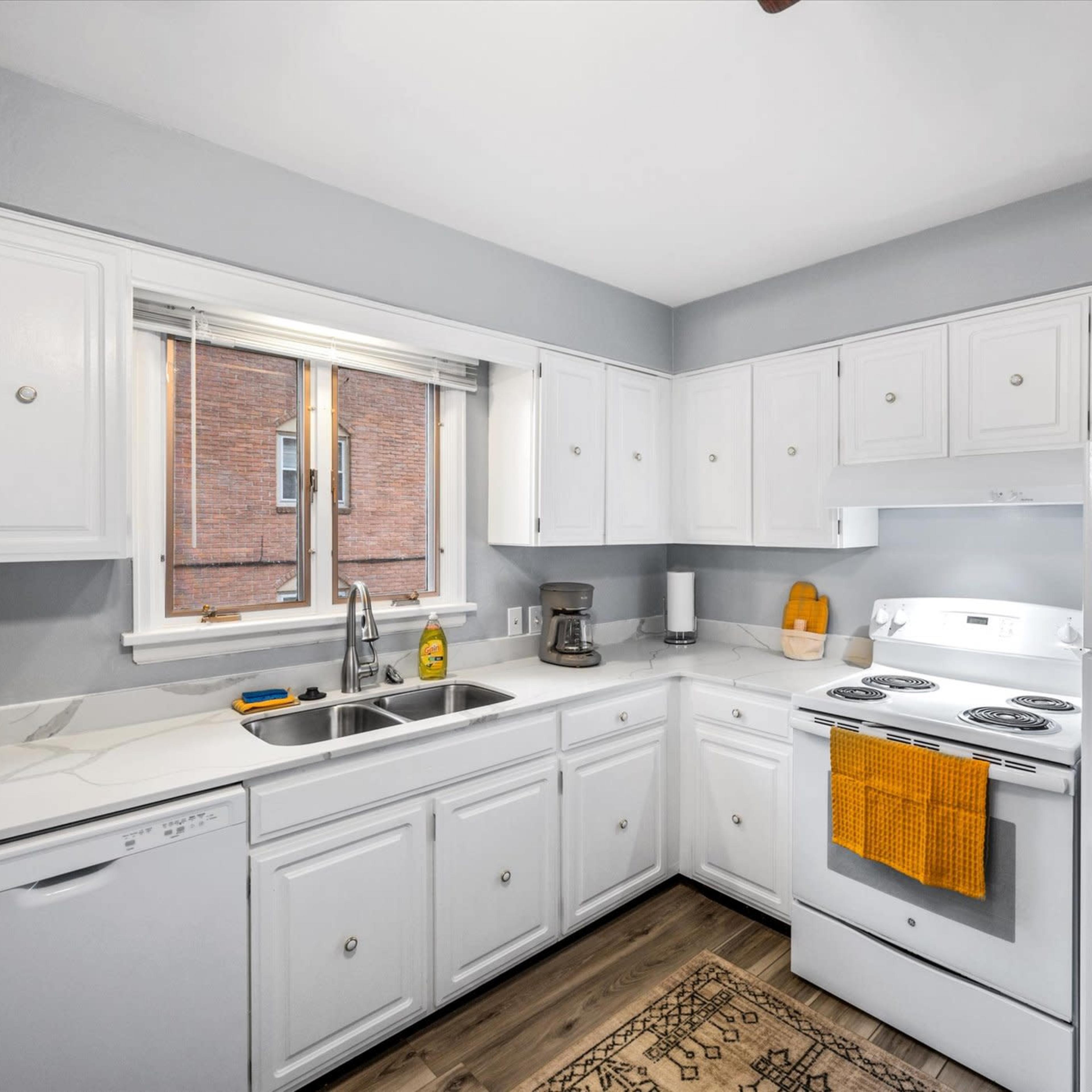 A clean kitchen with white cabinets, a white countertop, a window over the sink, and an oven with a stovetop.