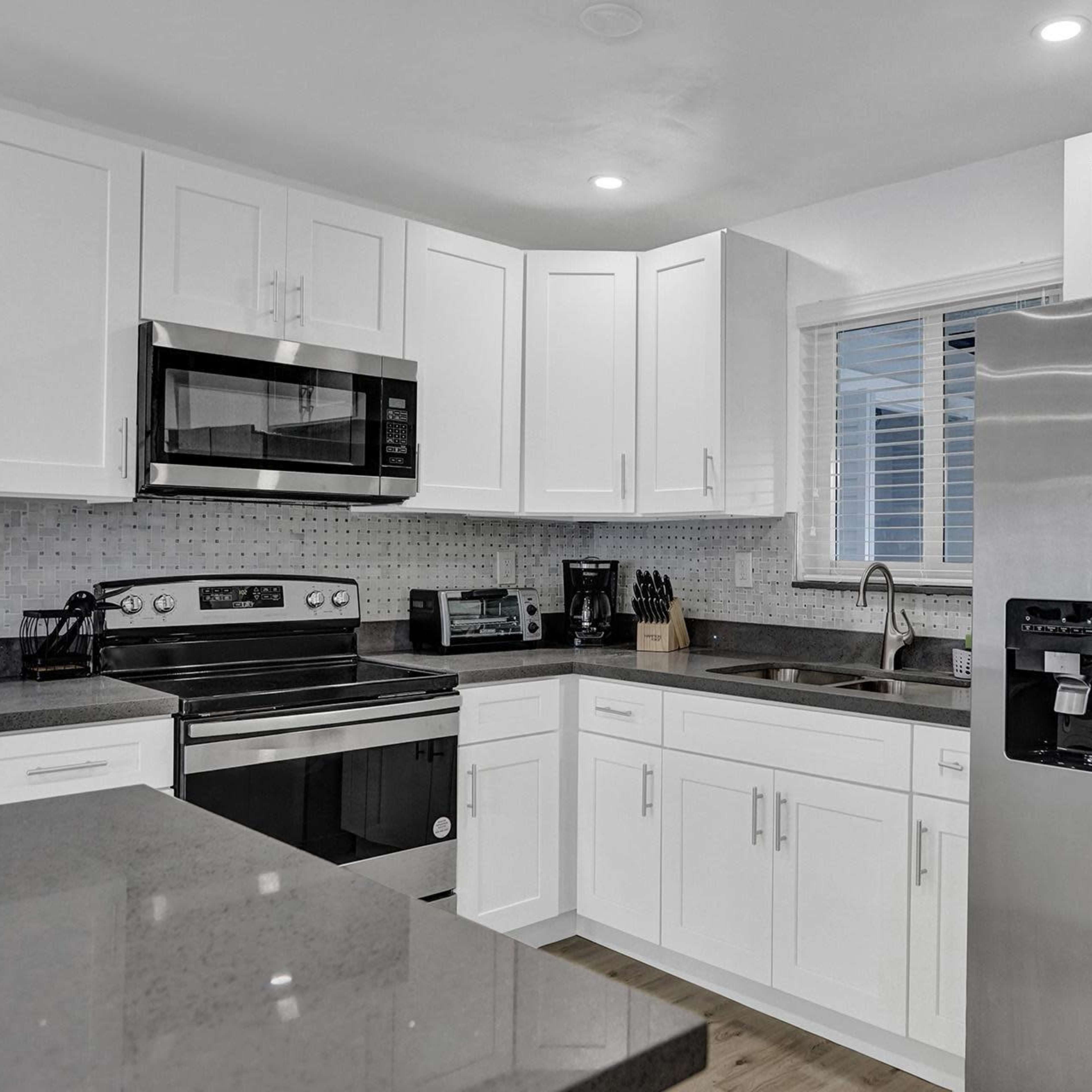 A modern kitchen features white cabinetry, stainless steel appliances, and a gray countertop.